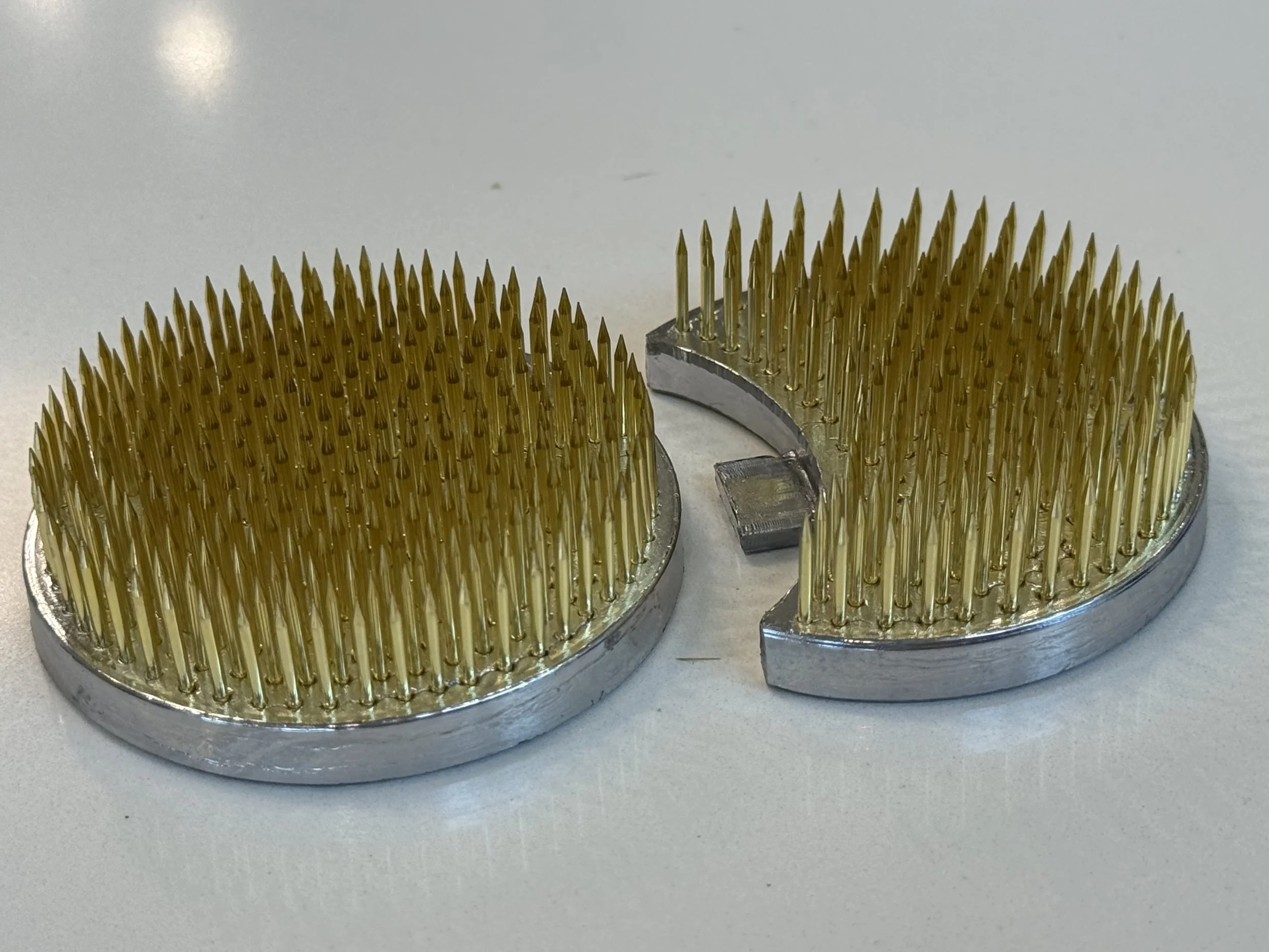Close-up of a cylindrical machine part with numerous gold-colored pins arranged in a circular pattern.