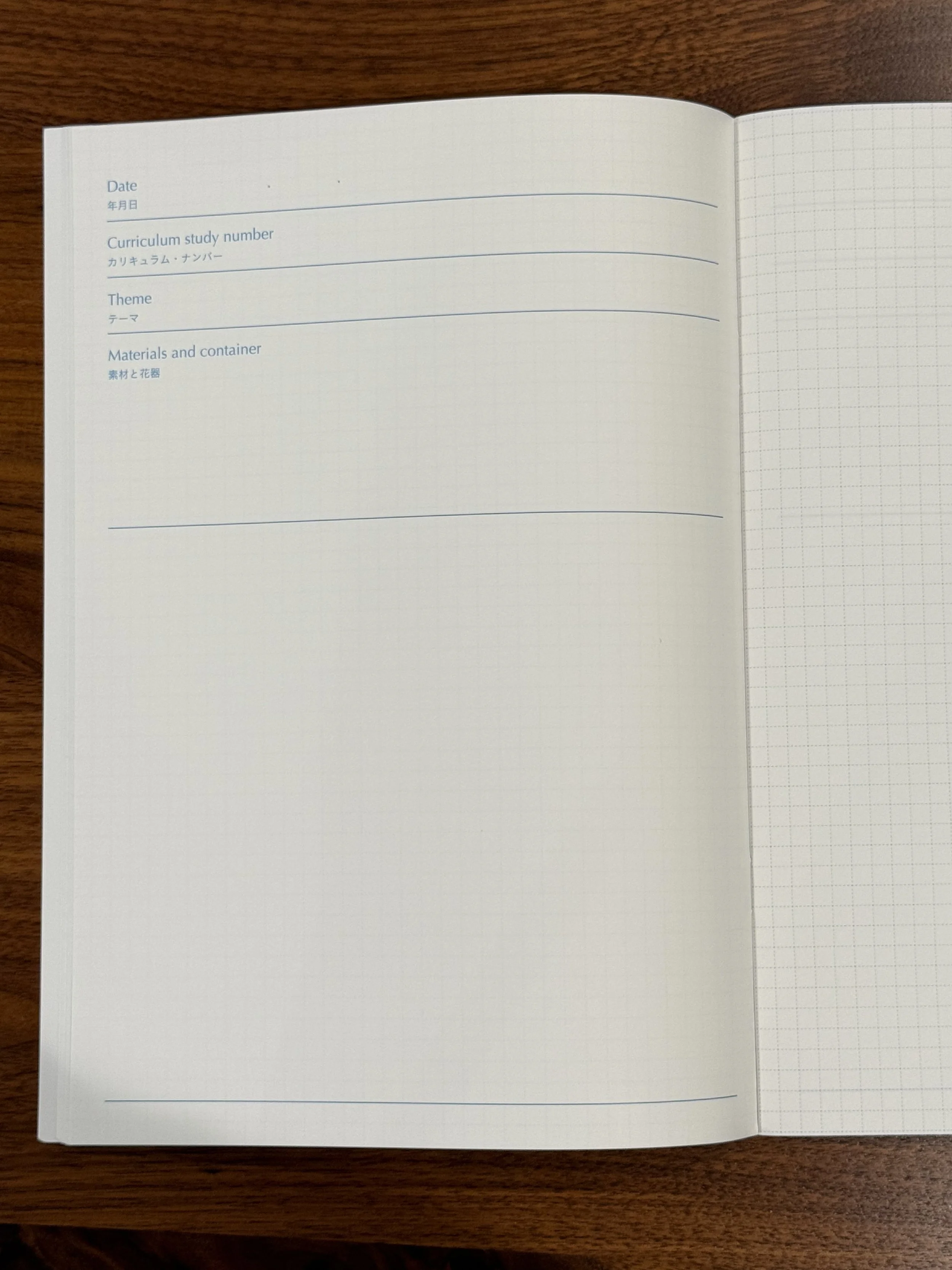 Open notebook on a wooden surface with pages showing sections for date, curriculum study number, theme, and materials and container, all written in English and Japanese.