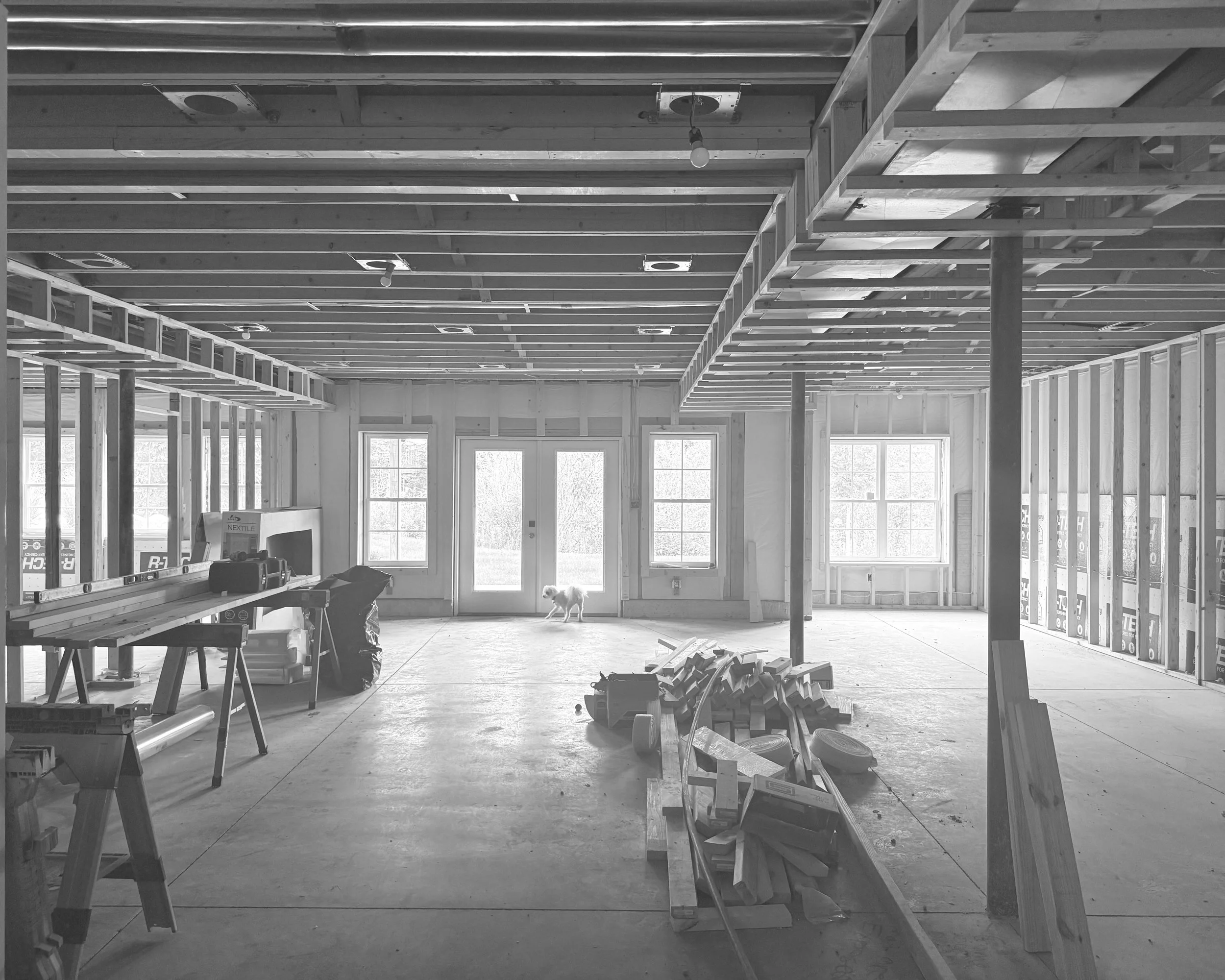 Interior of a house under construction with exposed ceiling joists, framing, and scattered construction materials, including tools and wood pieces.