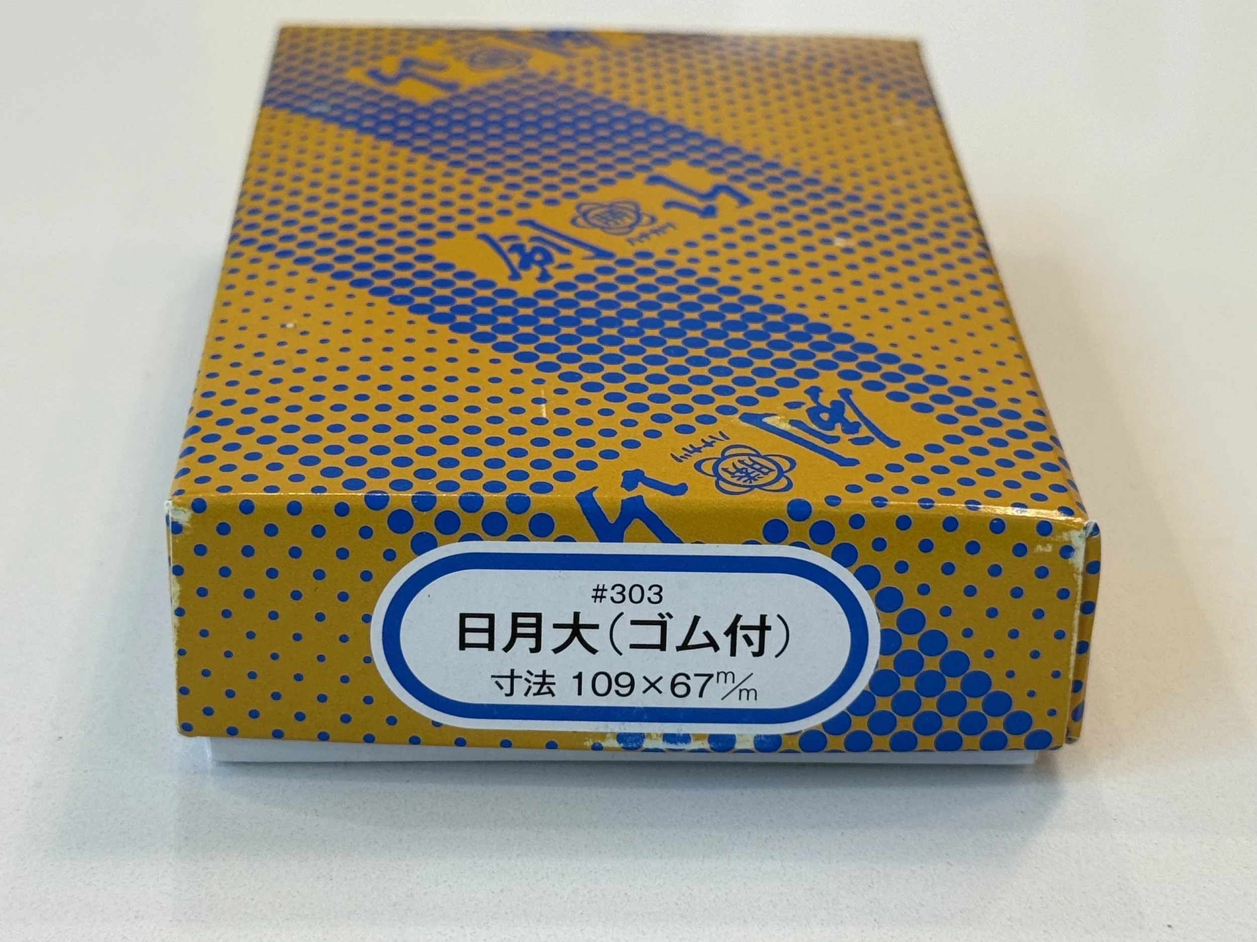 Close-up of a yellow and blue box with Japanese text and a logo, placed on a white surface.