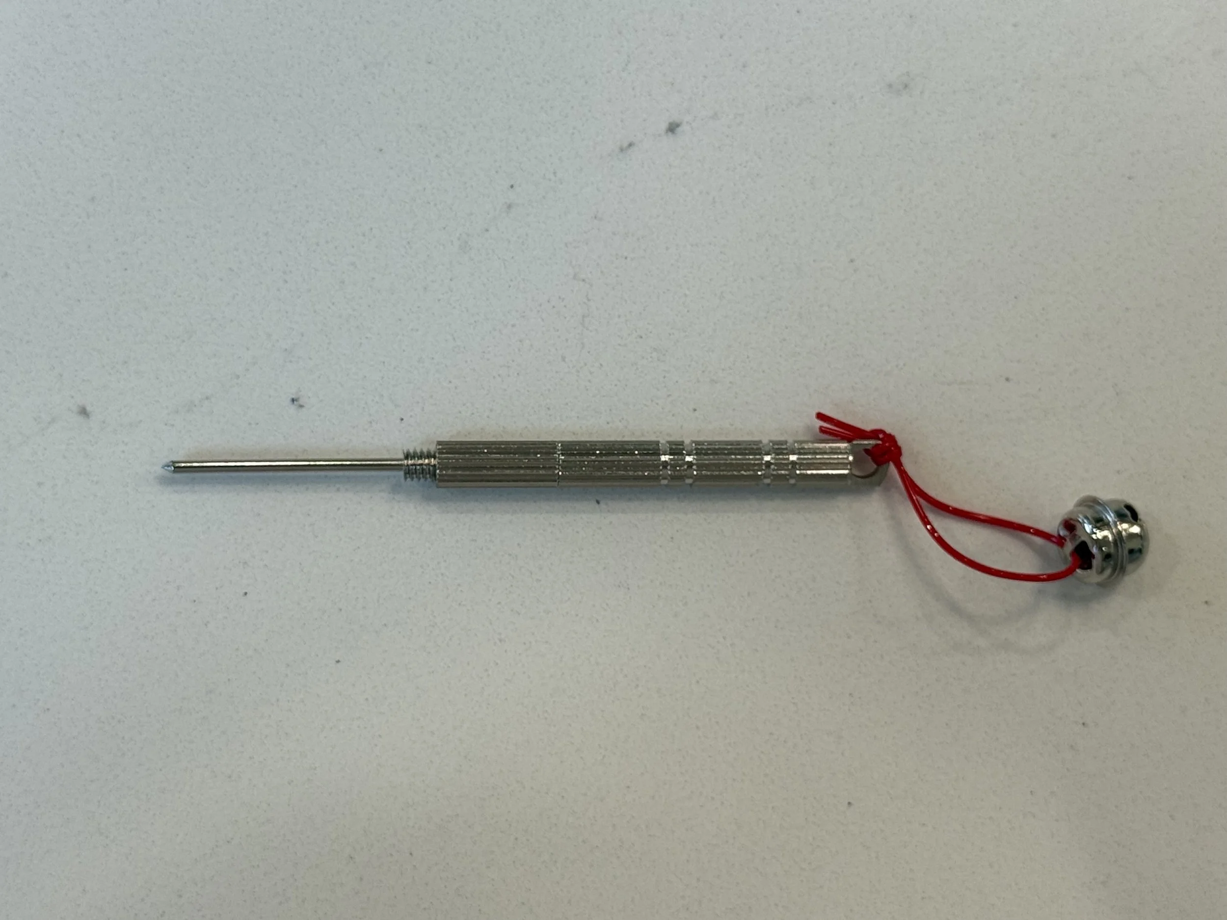 A metallic pen with a coiled spring tip and a red string tied to a small bell, placed on a white surface.