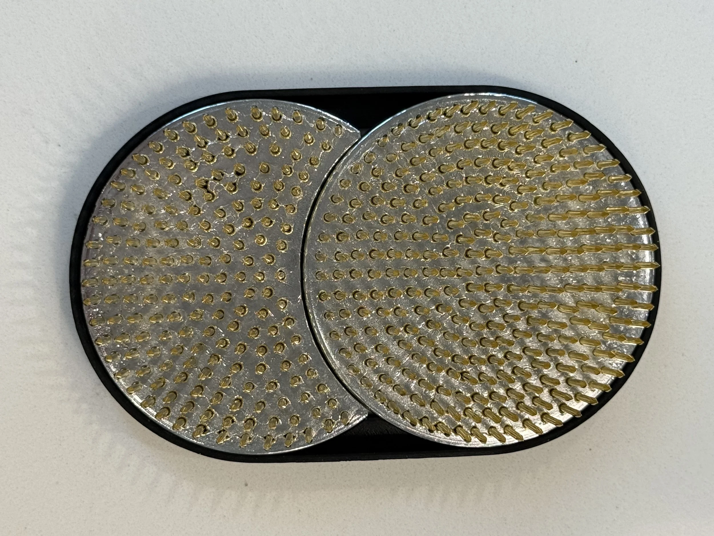 Close-up of a black circular nail drill bit holder containing two types of small, pointed gold nail drill bits, placed on a white surface.