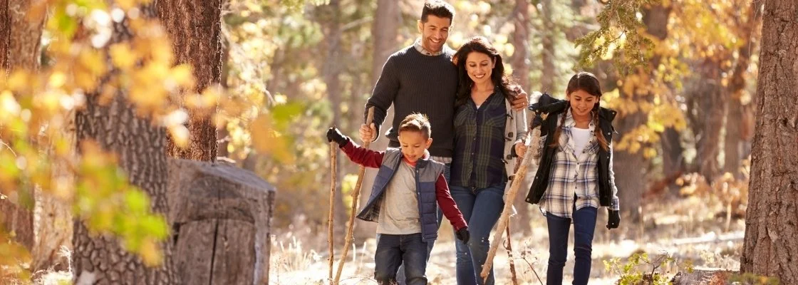 A family of four, two adults and two children, hiking in a forest during autumn.