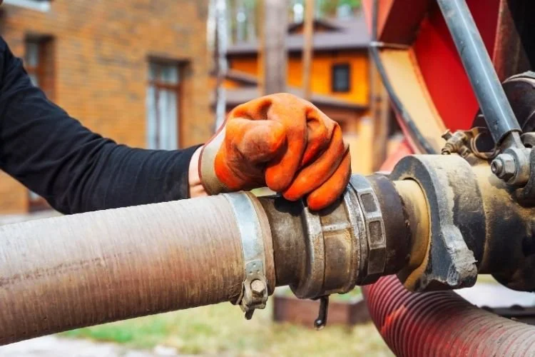 Close-up of a worker's hand, wearing an orange glove, gripping a large septic pipe.
