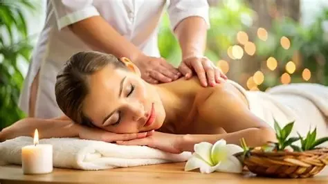 Woman lying face down receiving a massage in a spa setting with lit candle and flowers nearby.