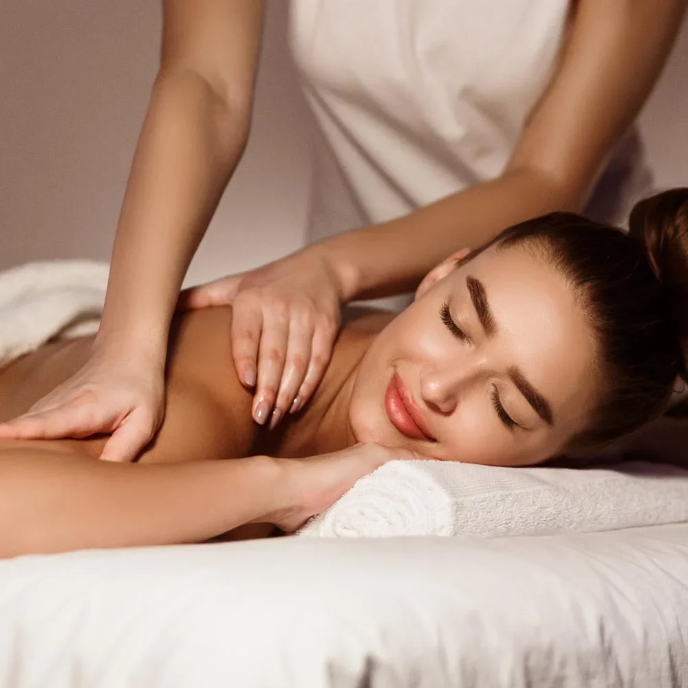 A woman receiving a massage on her back, lying face down on a massage table, with a massage therapist applying pressure with hands.