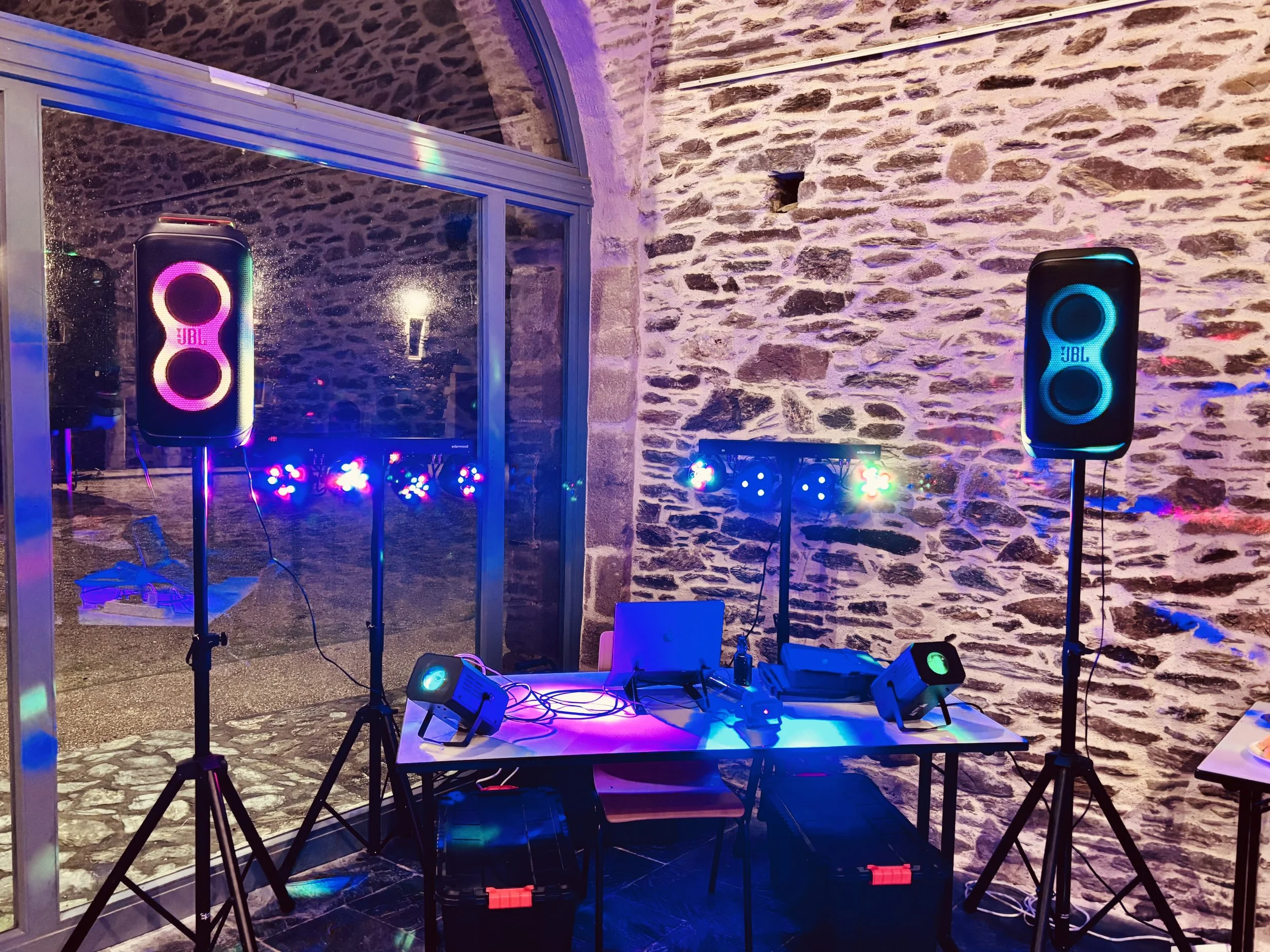 Sonorisation DJ avec haut-parleurs JBL lumineux, lumières colorées, matériel audio et décor en pierre, ambiance festive