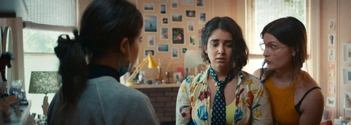 Two women talking to a third woman in a cozy, decorated room with photos on the wall.