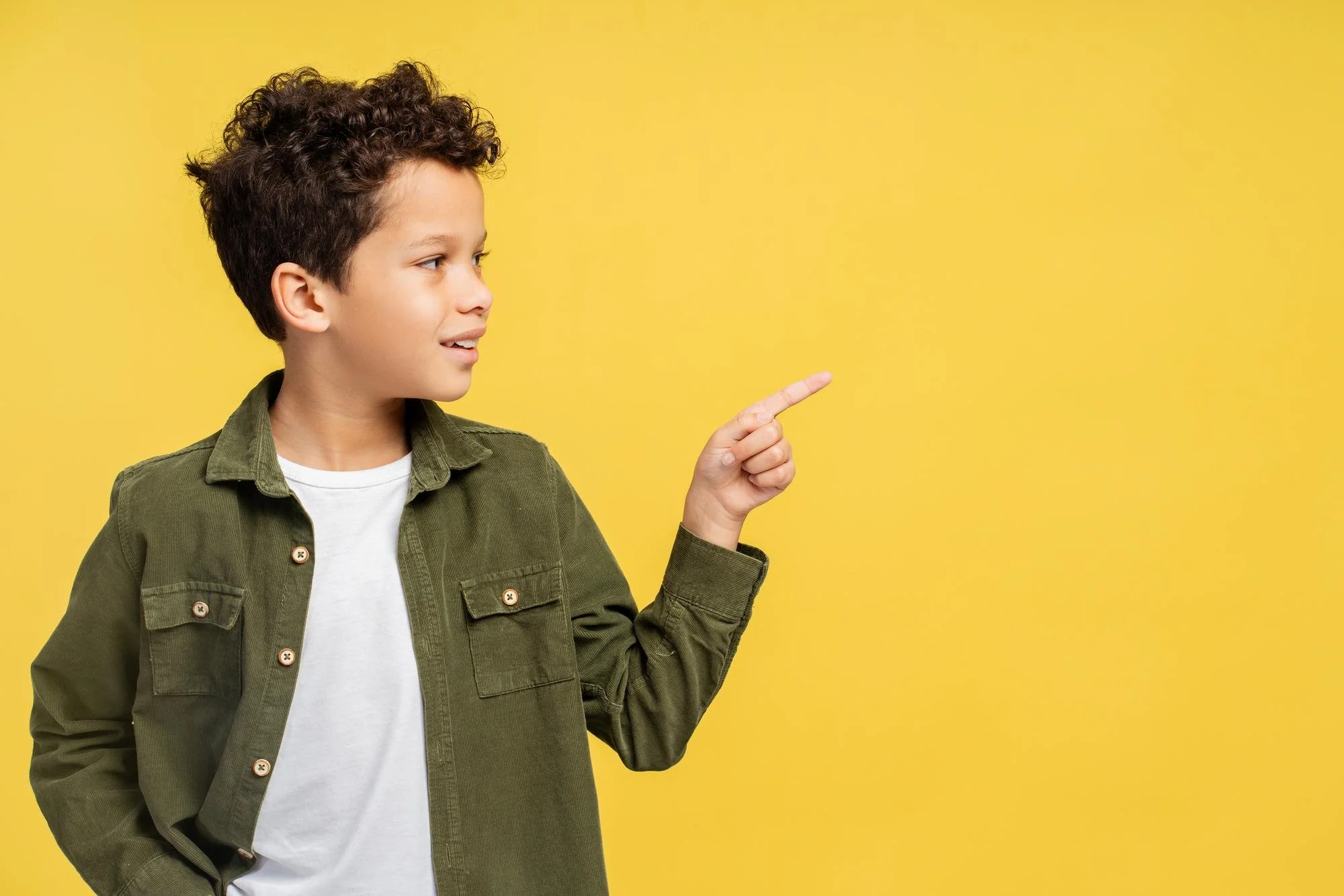 Ragazzo con maglietta bianca e giacca verde che indica un punto sulla parete gialla accanto a lui.