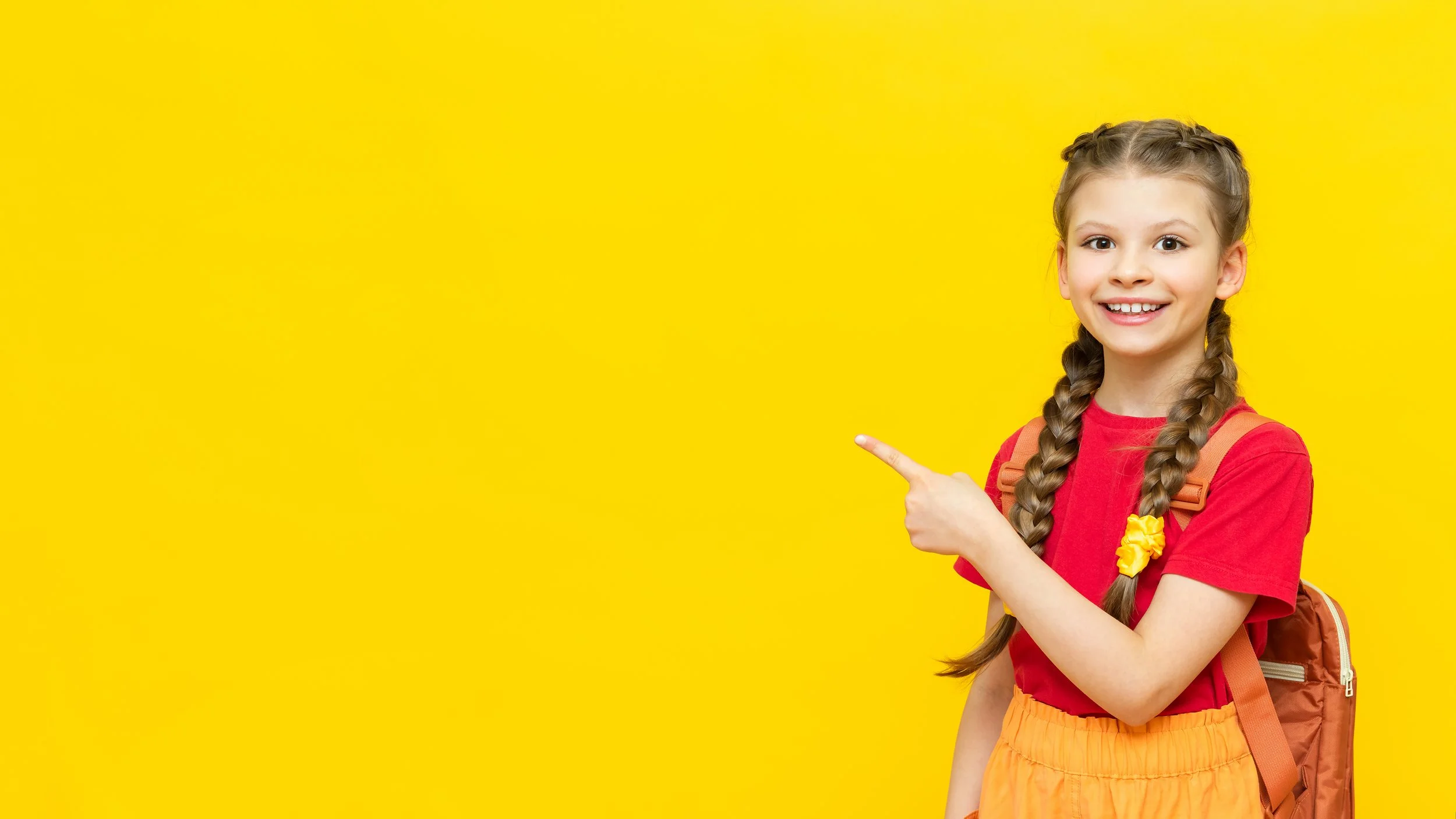 Una ragazza sorridente con treccine, indossa una maglietta rossa, pantaloncini arancioni e una cartella marrone, e indica verso sinistra su uno sfondo giallo.