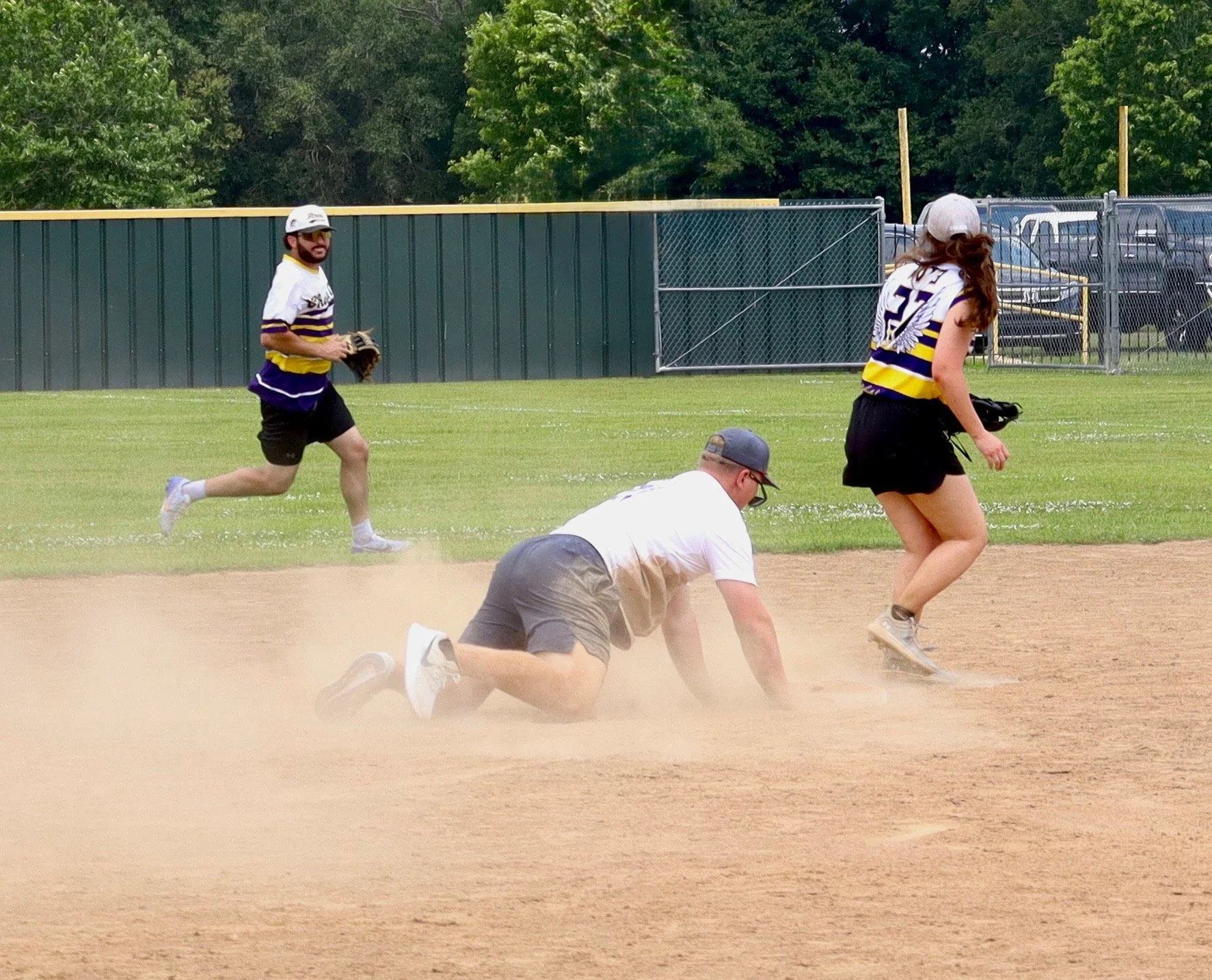 People playing baseball on a field, with one person sliding into a base, while others are running or waiting nearby.