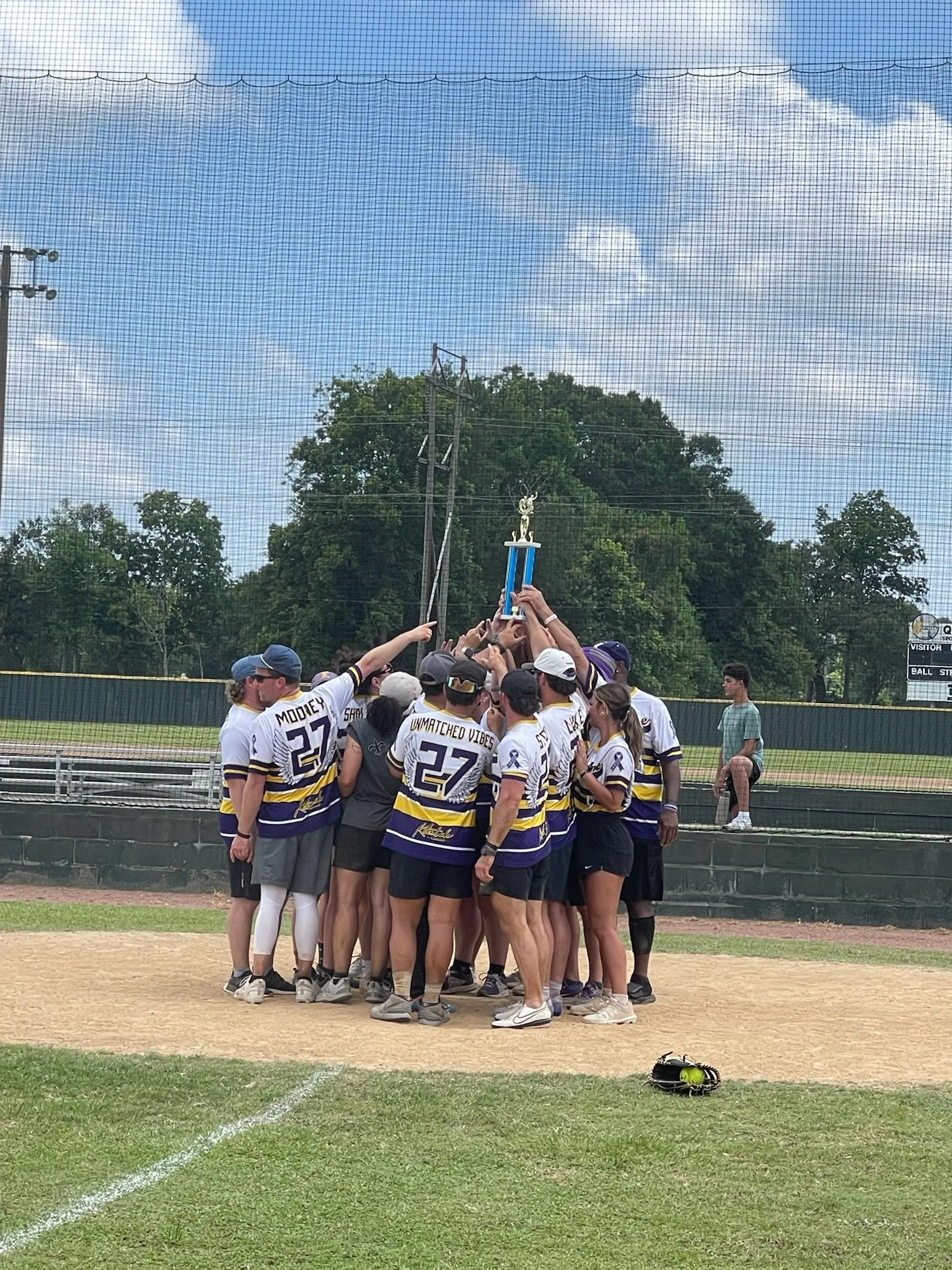 Group of softball players celebrating and holding a trophy on the field.