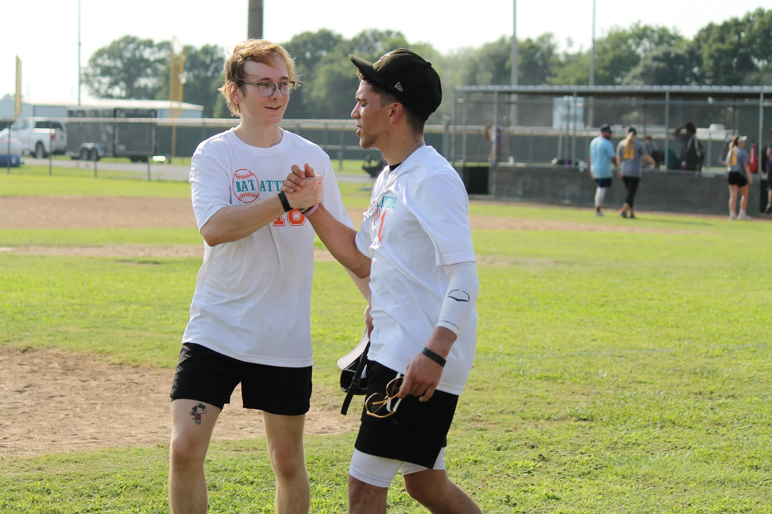 Two young men on a baseball field shaking hands and exchanging high fives after a game, with others in the background.