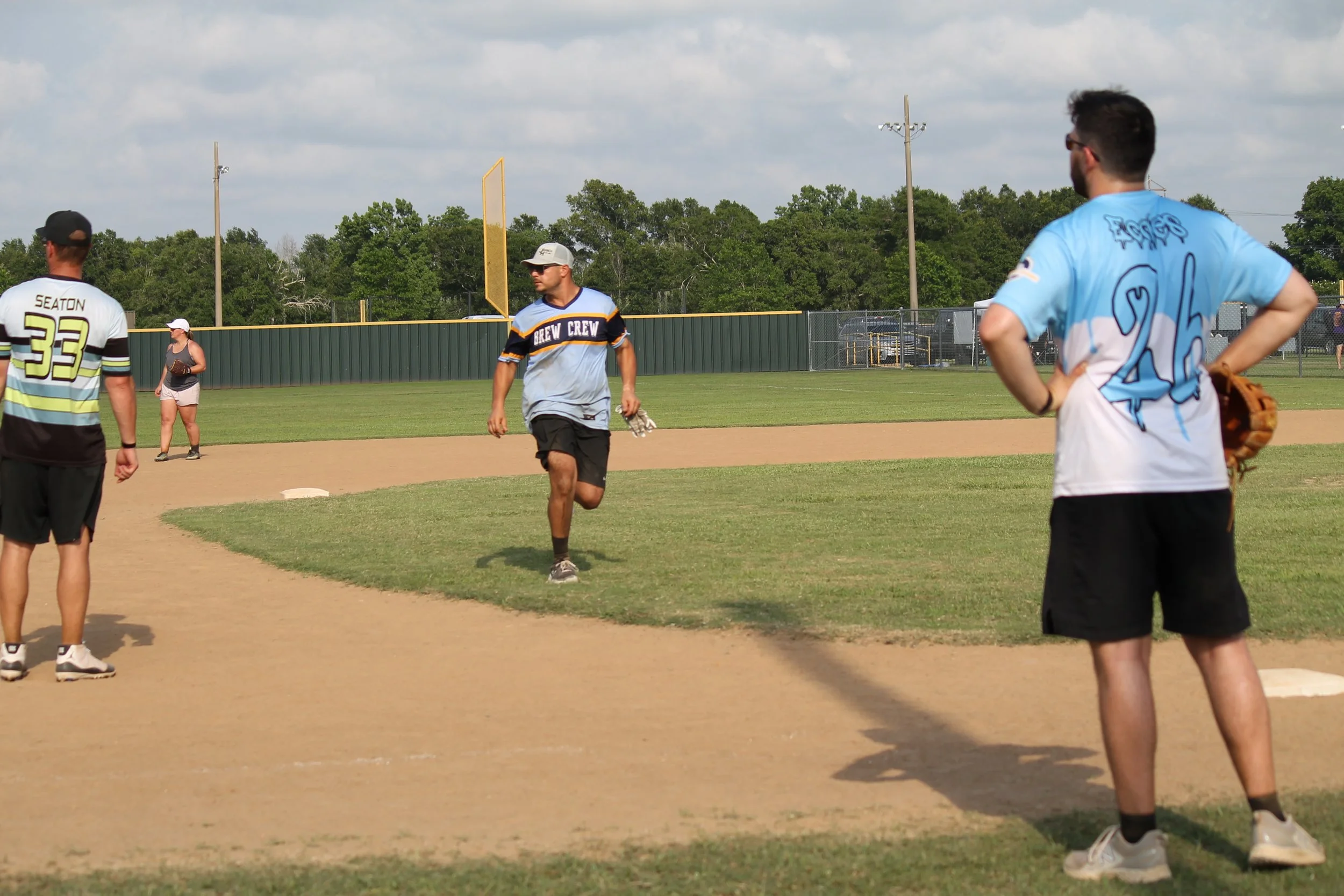 People playing baseball on a field under a partly cloudy sky.