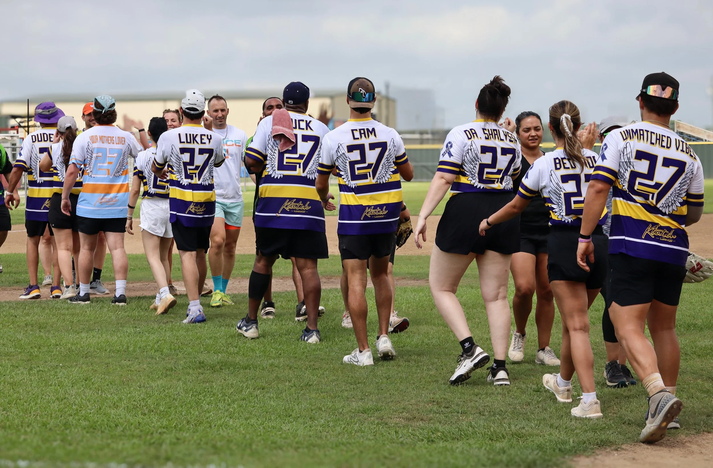 Group of people on a grass field wearing sports jerseys with the number 27.