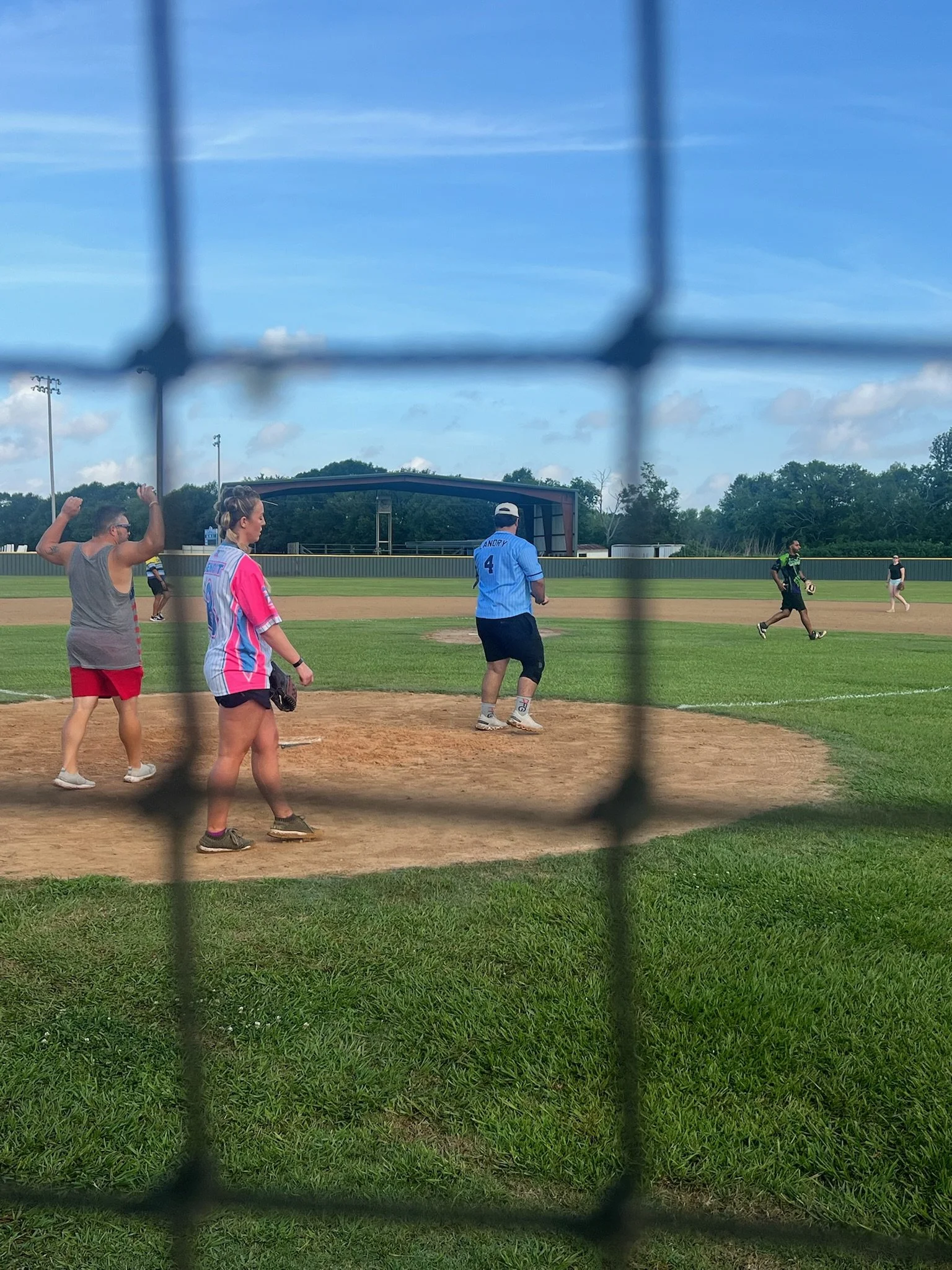 People playing baseball on a field viewed through a chain-link fence.