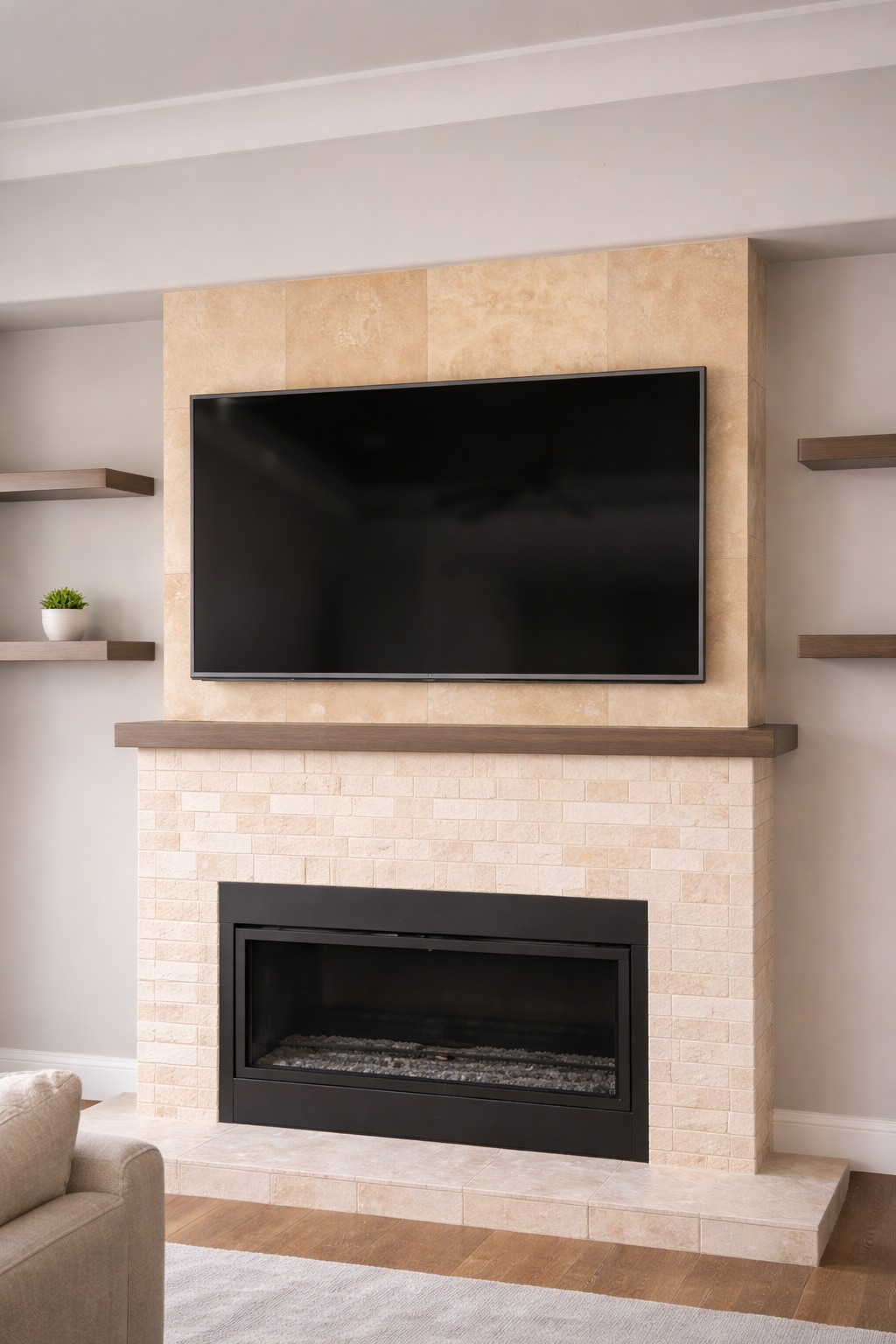 Living room with television mounted above a fireplace with a brick surround, wooden mantel, and decorative beige tiles, flanked by floating wooden shelves on light gray walls.