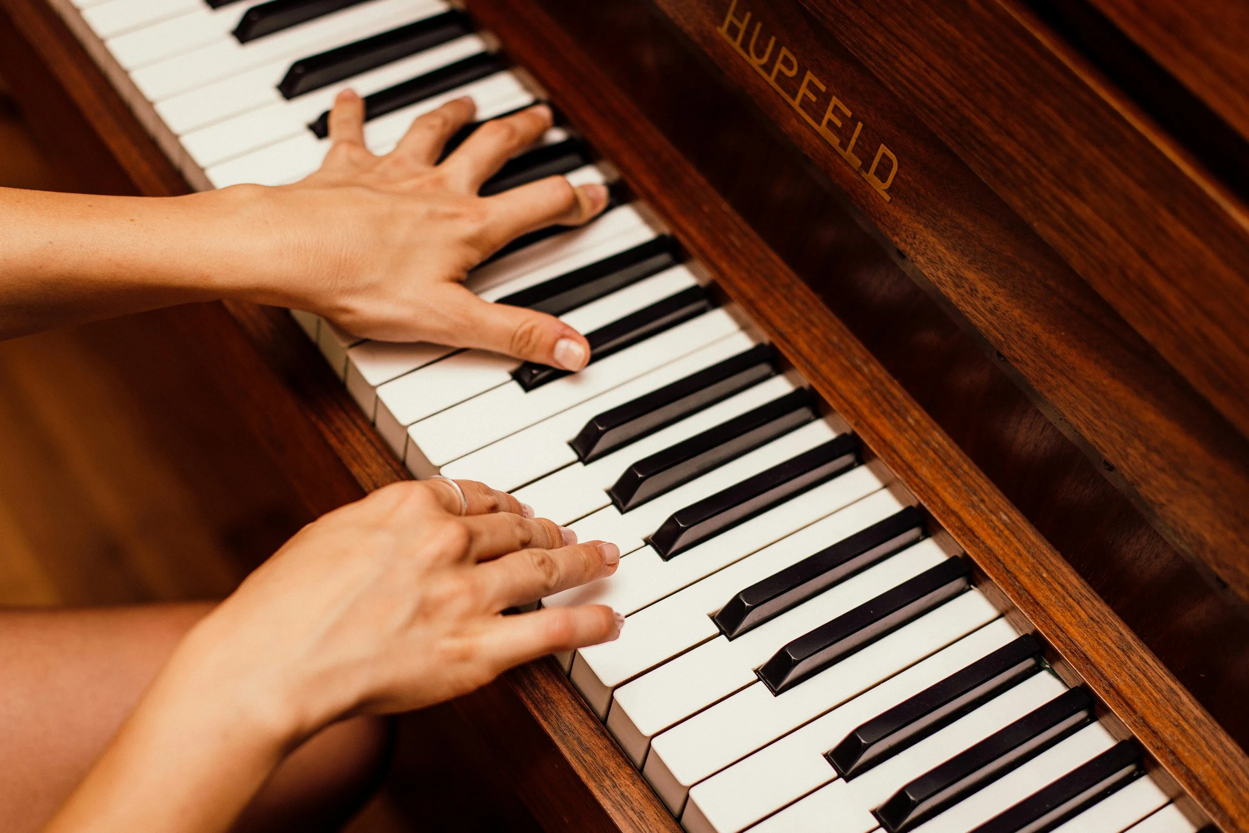 Someone playing a wooden upright piano with black and white keys.
