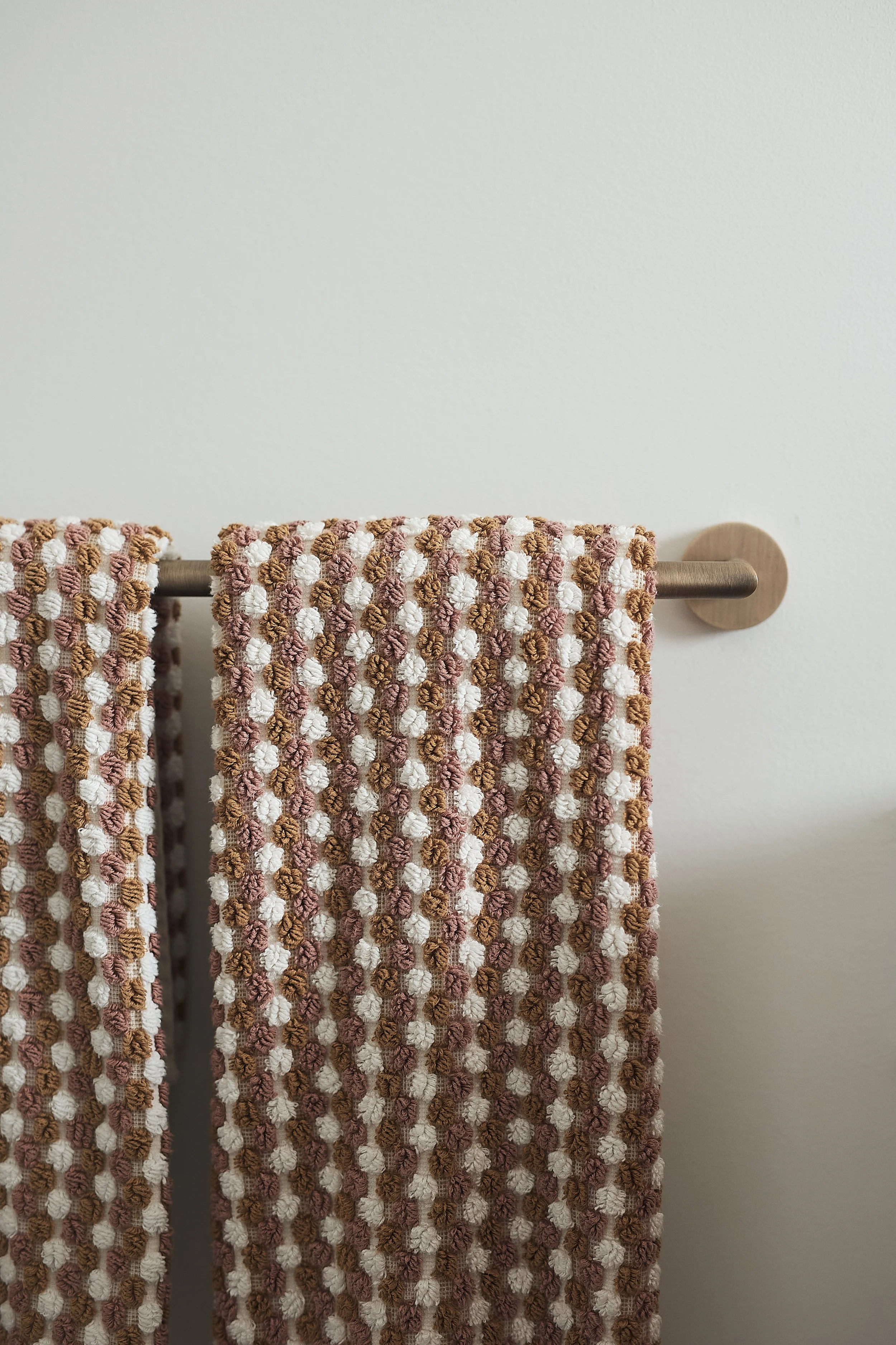 Close-up of two textured, patterned towels hanging on a brass towel rack mounted on a plain wall.