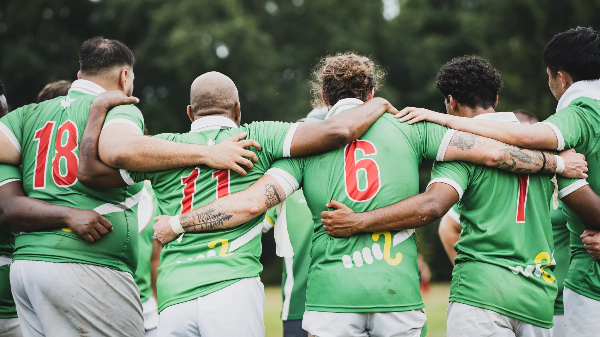 A group of soccer players in green jerseys huddle together on a field, arms around each other's shoulders, moment of team unity.