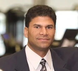 A man wearing a suit and tie, posing for a professional portrait in an office setting.