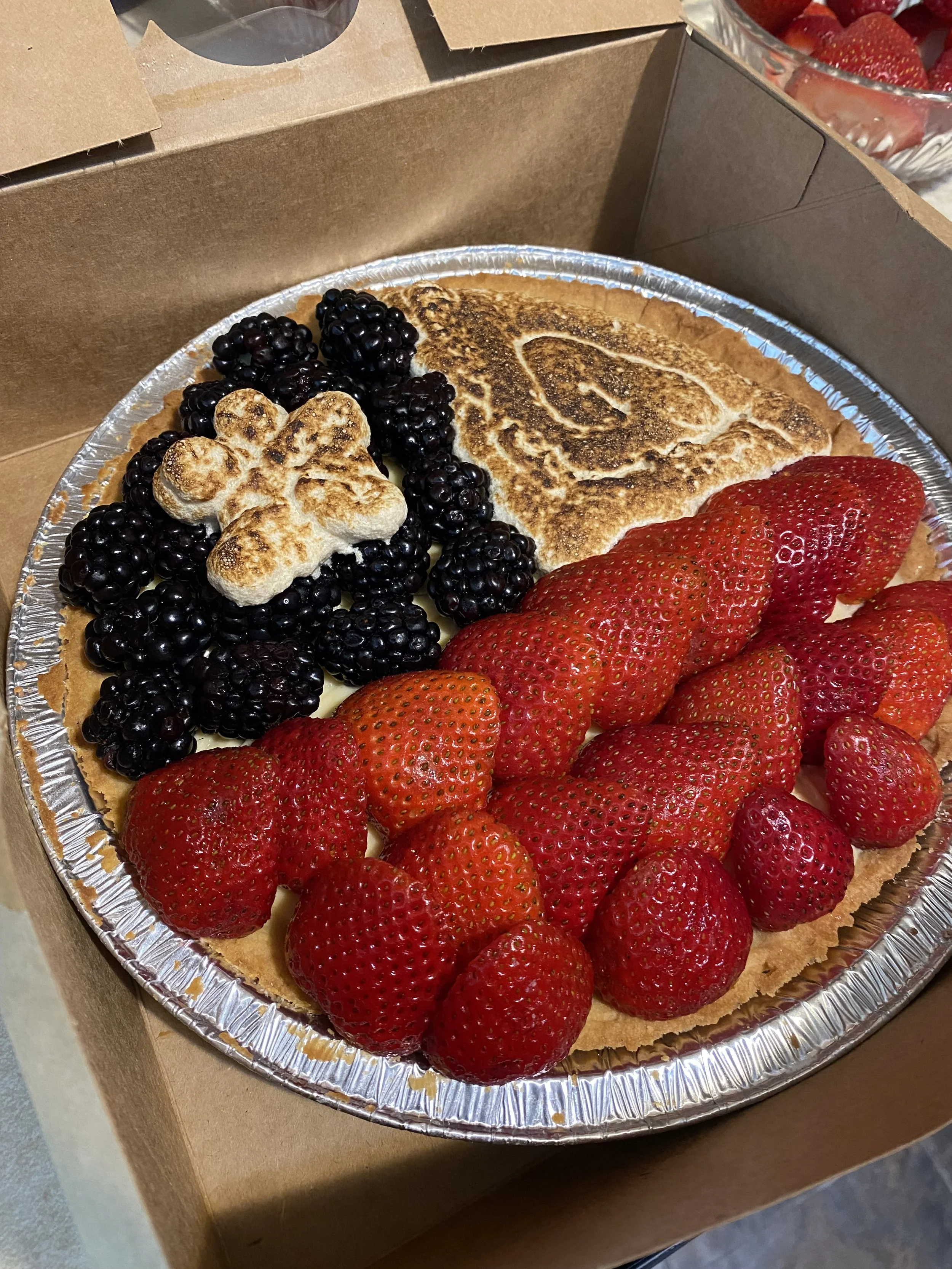 A fruit tart topped with fresh strawberries, blackberries, and a heart-shaped marshmallow on a graham cracker crust.