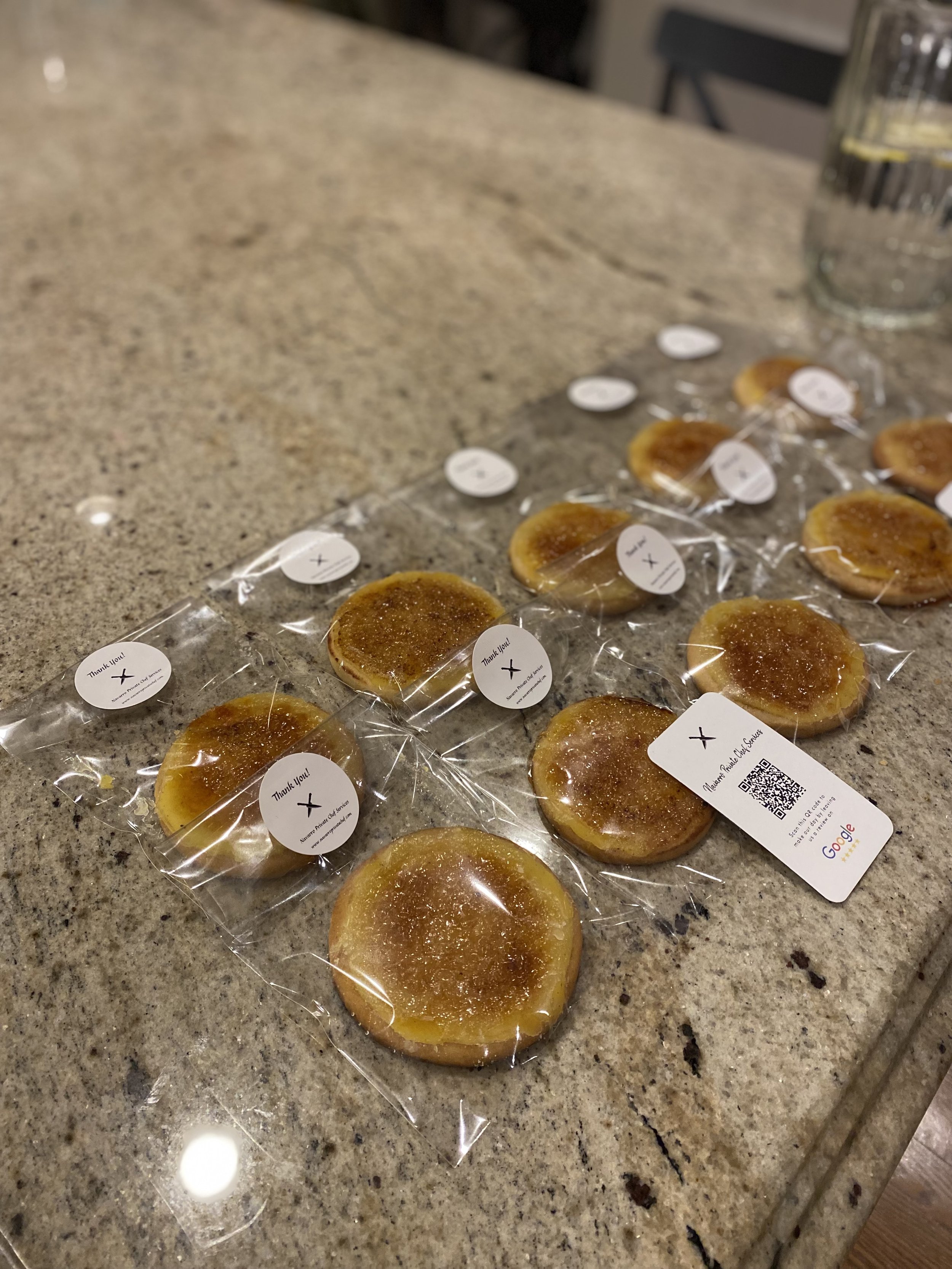 Multiple individually wrapped caramel candies on a granite countertop, with a glass of water and a chair in the background.