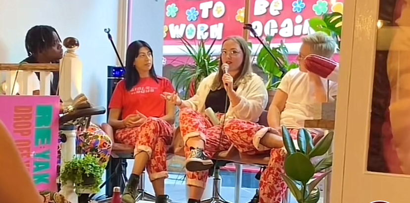 Four people sitting in a circle during a discussion or presentation, inside a colorful room with plants and bright signage that reads 'To be worth' and 'To be great.'