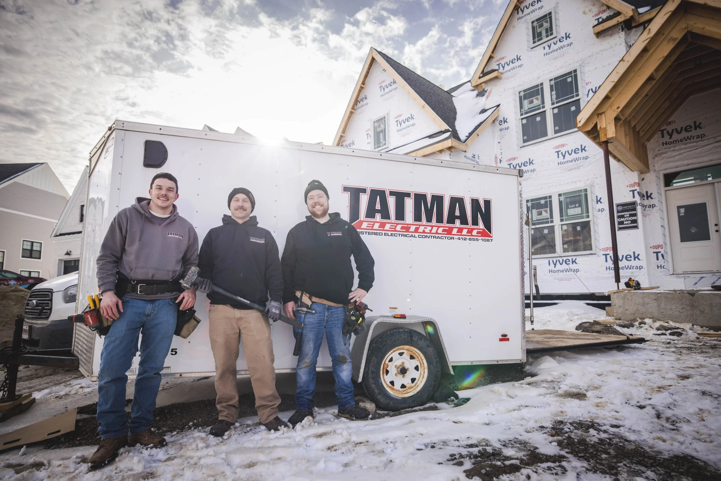 Tatman Electric LLC crew standing in front of branded work trailer at snowy residential job site Pittsburgh PA