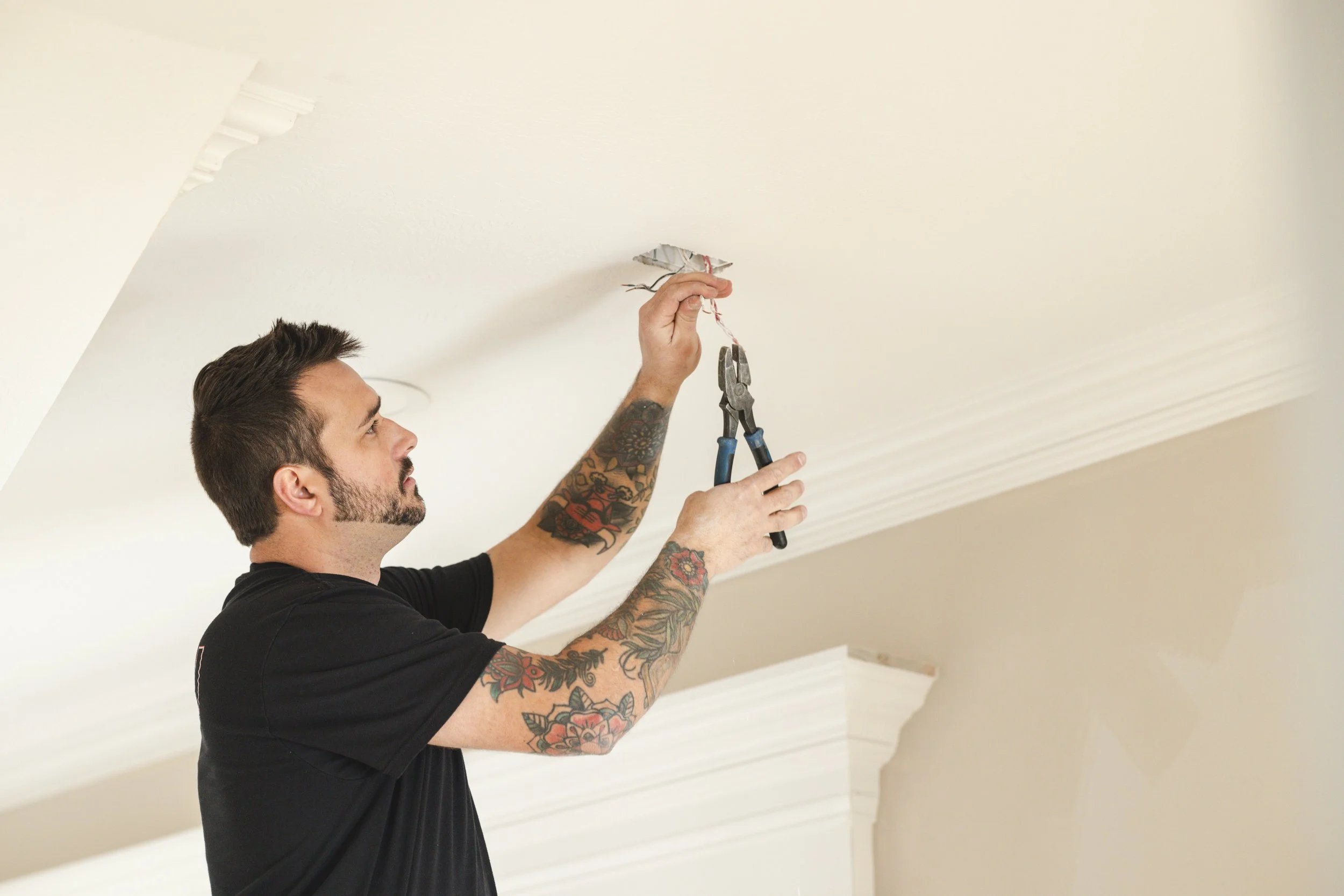 A man with tattoos is repairing a hole or damage in a white ceiling using pliers and a piece of repair patch.