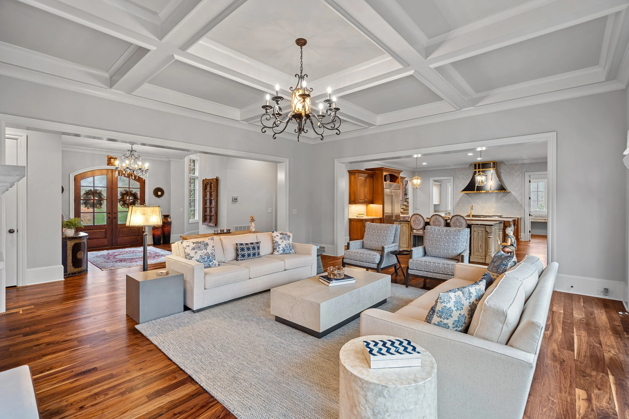Living room with white sofas, armchairs, a coffee table, hardwood floors, and a chandelier.