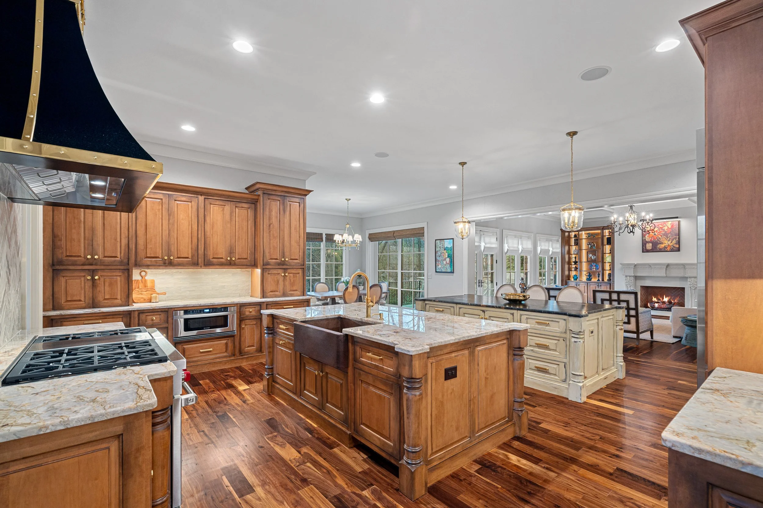 Spacious kitchen with wooden cabinets, marble countertops, and hardwood floors, open to a living area with fireplace and large windows.