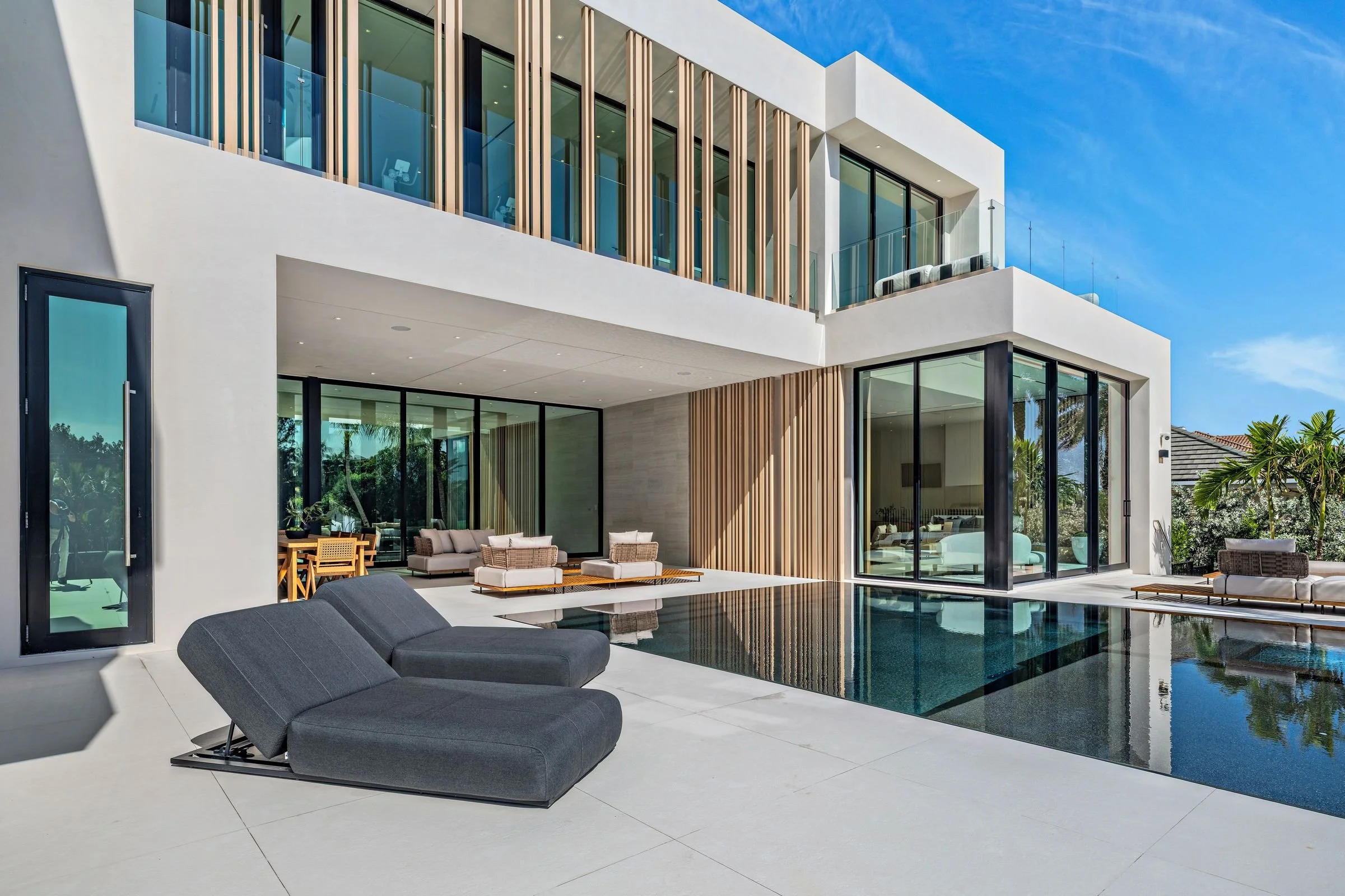 Modern house with a swimming pool, outdoor lounge chairs, and large glass windows and doors