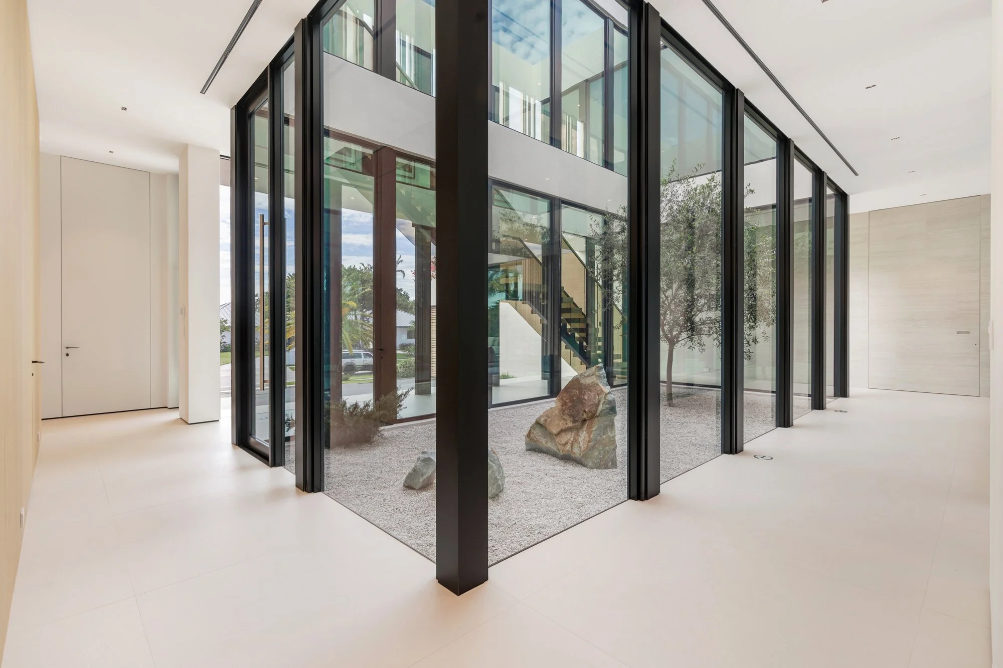 Modern interior space with a glass-enclosed courtyard featuring rocks and gravel, surrounded by white walls and large windows.