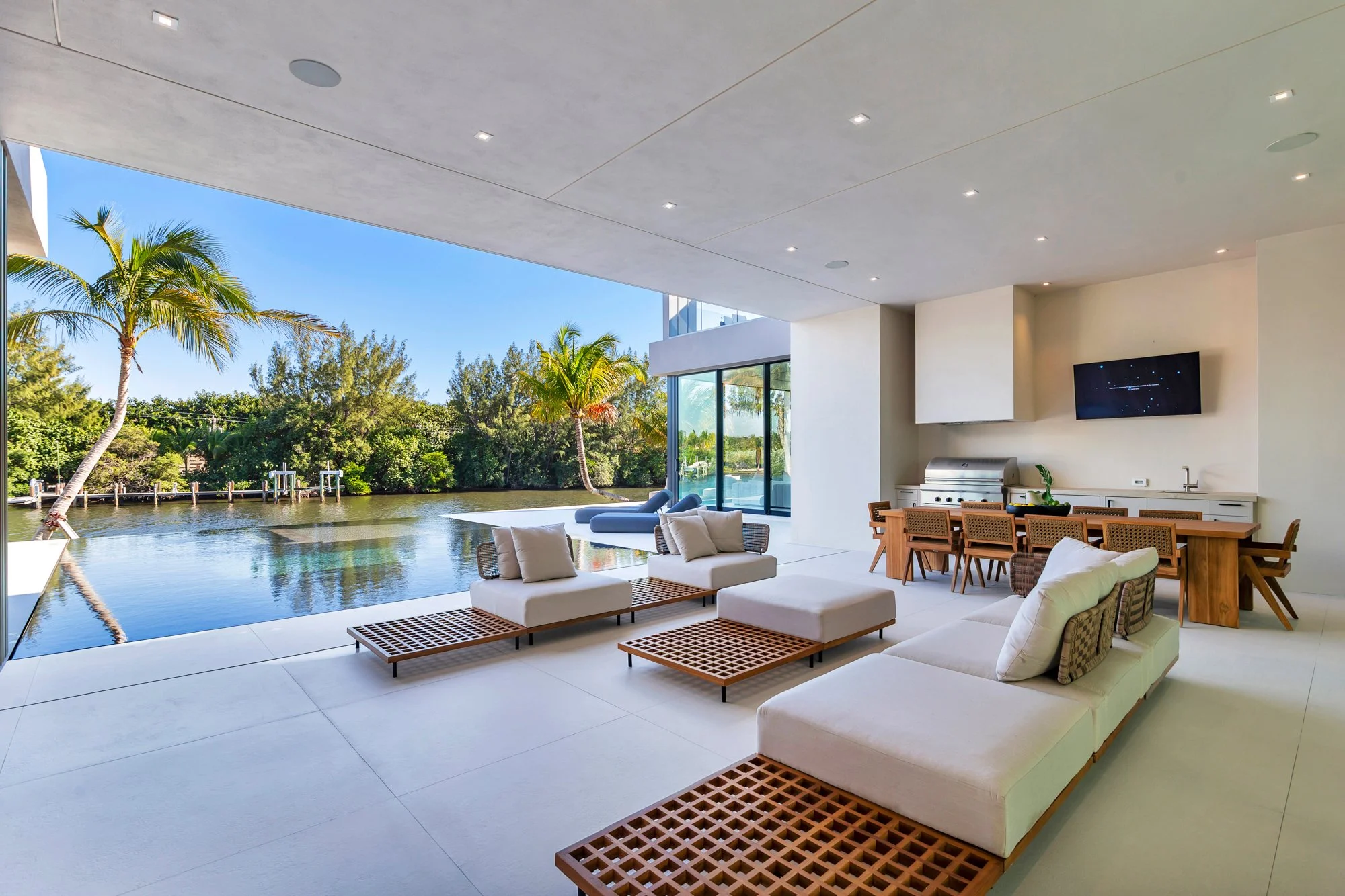 Modern outdoor living space with white seating and a view of a river and tropical trees.