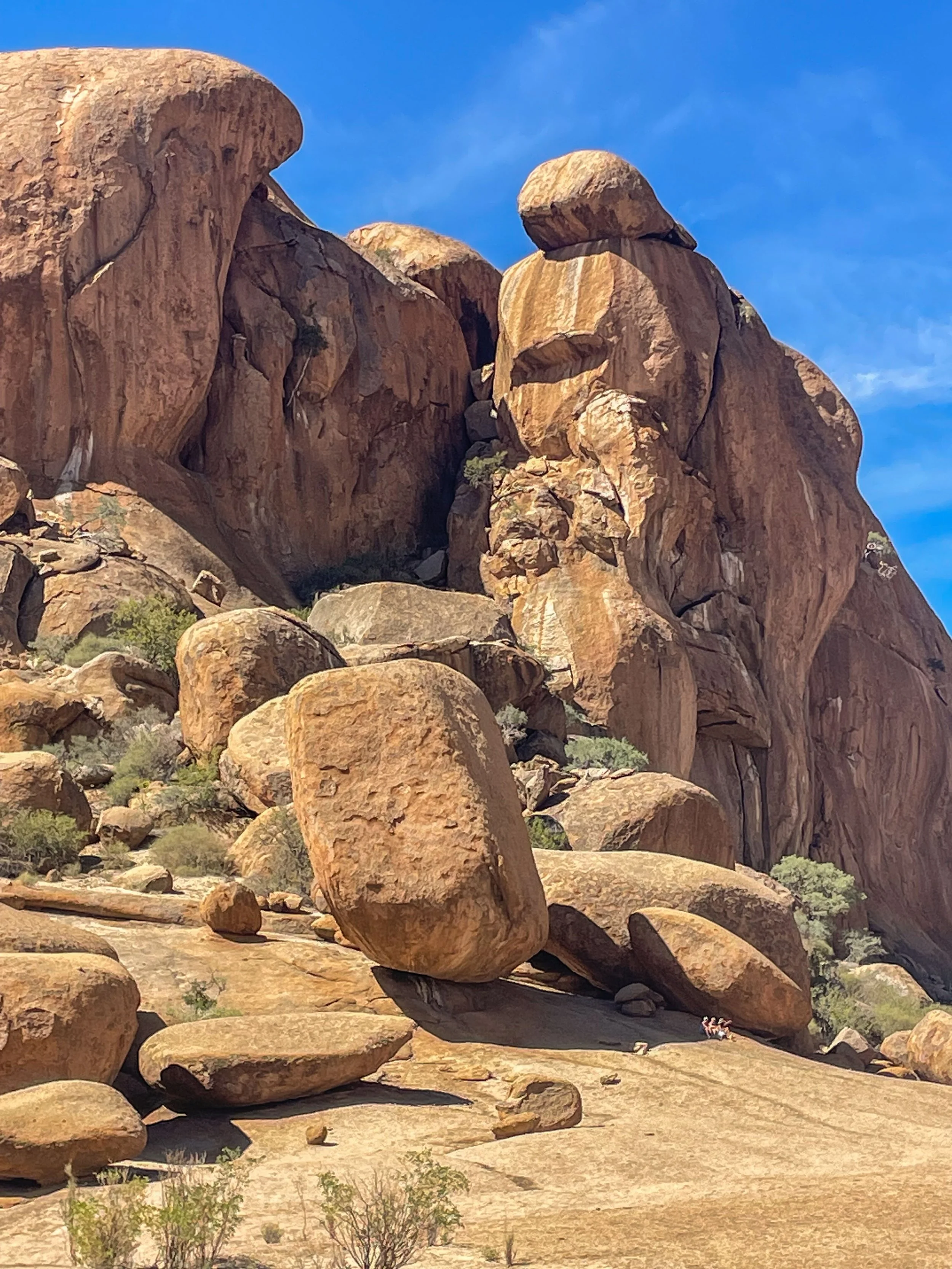 Großer Felsen- und Steinformationen in einer Wüste, mit einigen kleinen Büschen, unter einem blauen Himmel. Erongo region namibia, damaraland