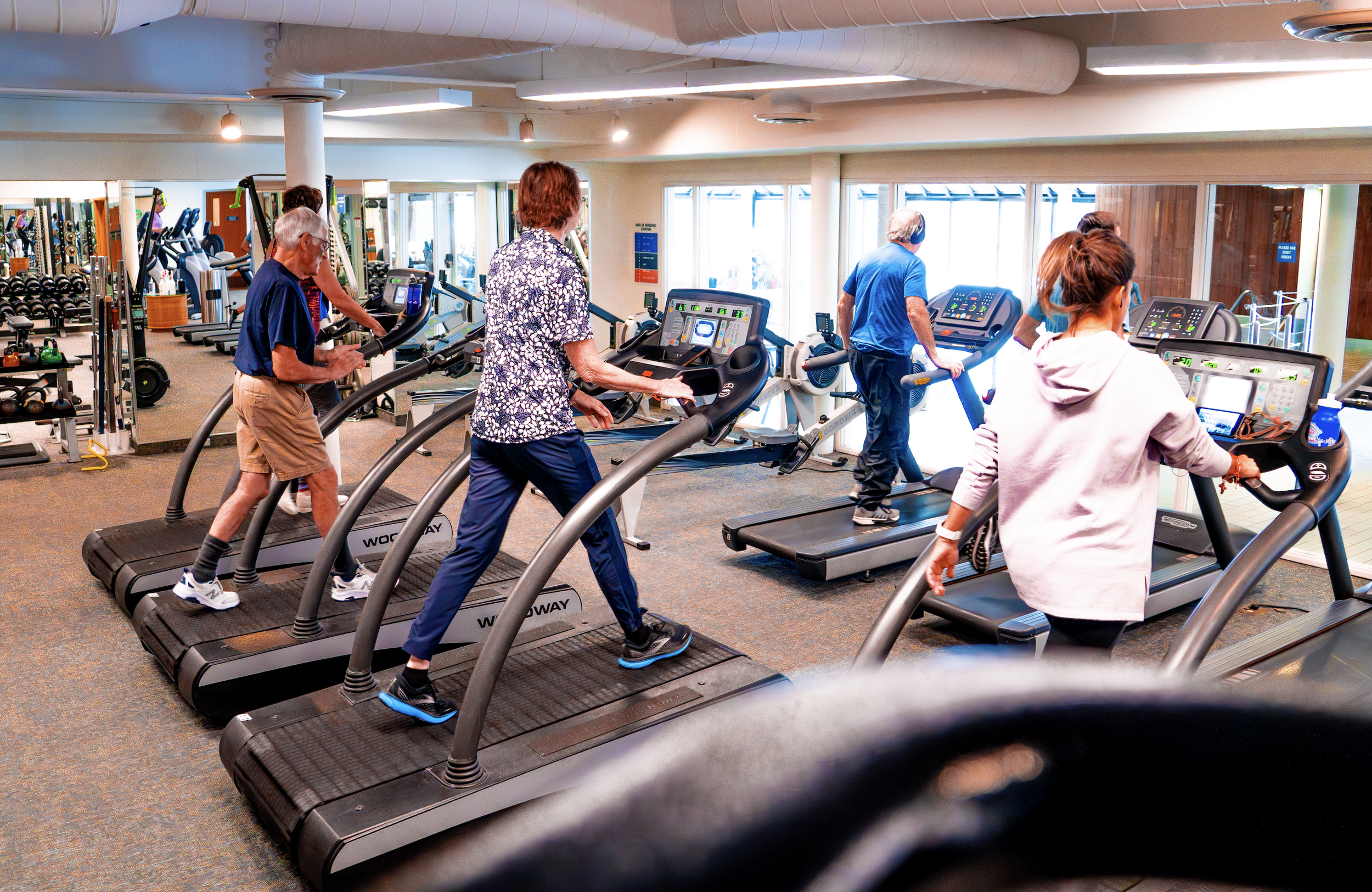 People exercising on treadmills in a gym, with additional workout equipment and mirrors in the background.