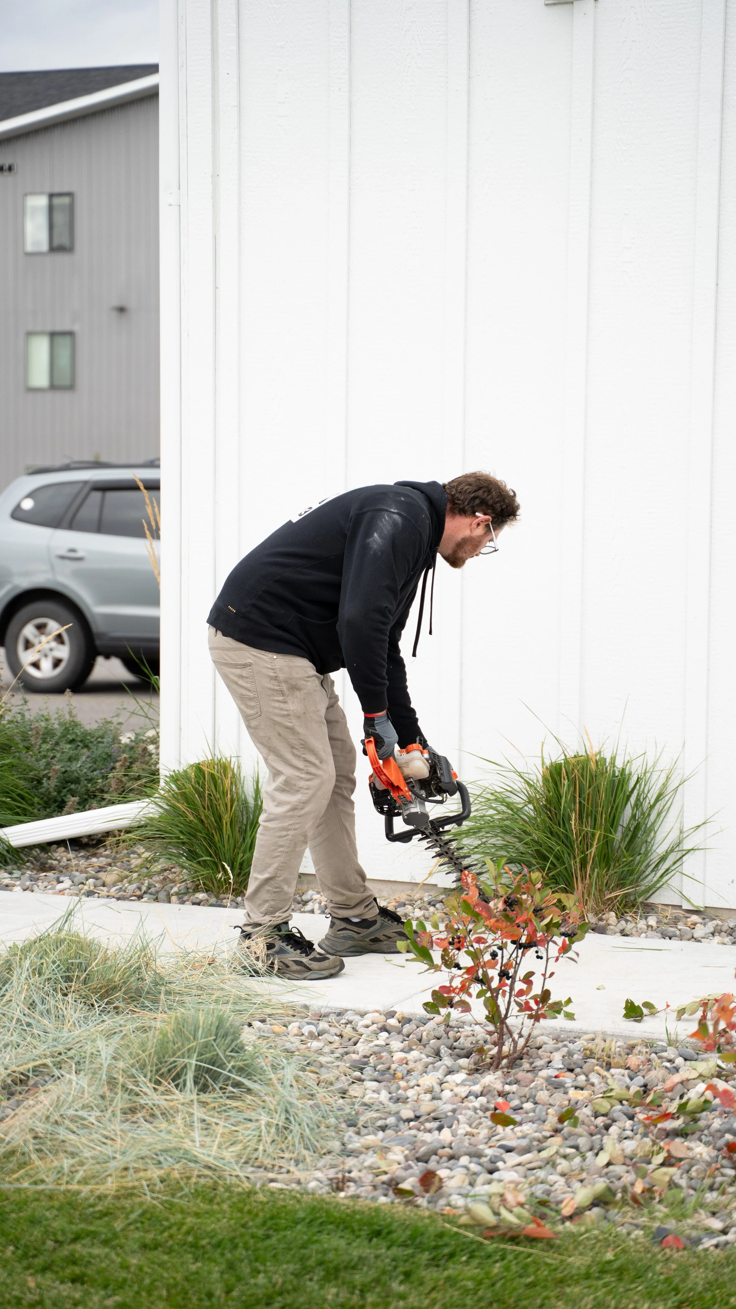 A man using a power auger to plant a shrub in a landscaped yard outside a building.