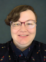A person with short curly brown hair, wearing glasses and a collared shirt with a dark background.