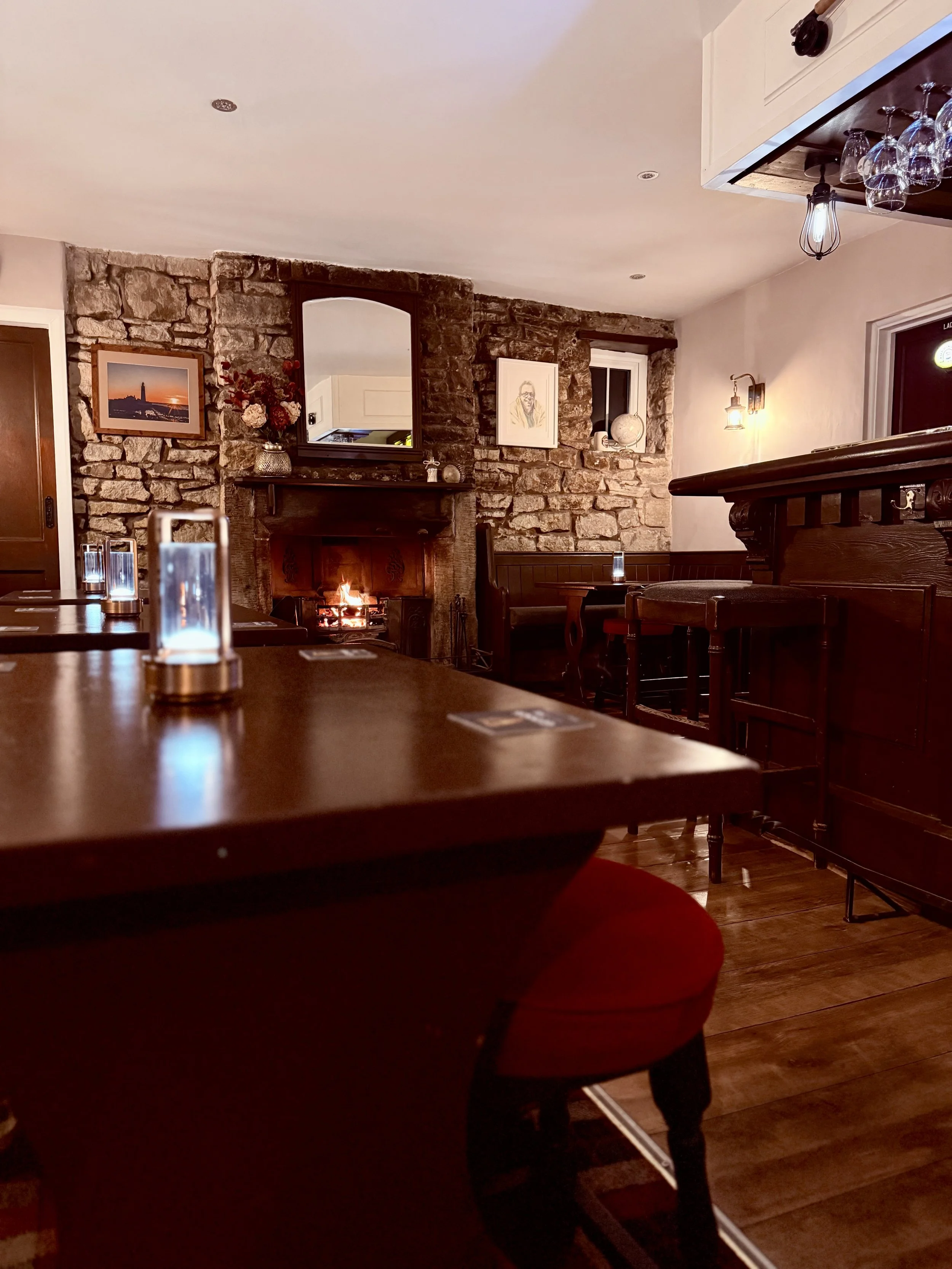 Cozy dining area with wooden furniture, a stone fireplace, and wall art, illuminated by warm lighting, creating inviting atmosphere.