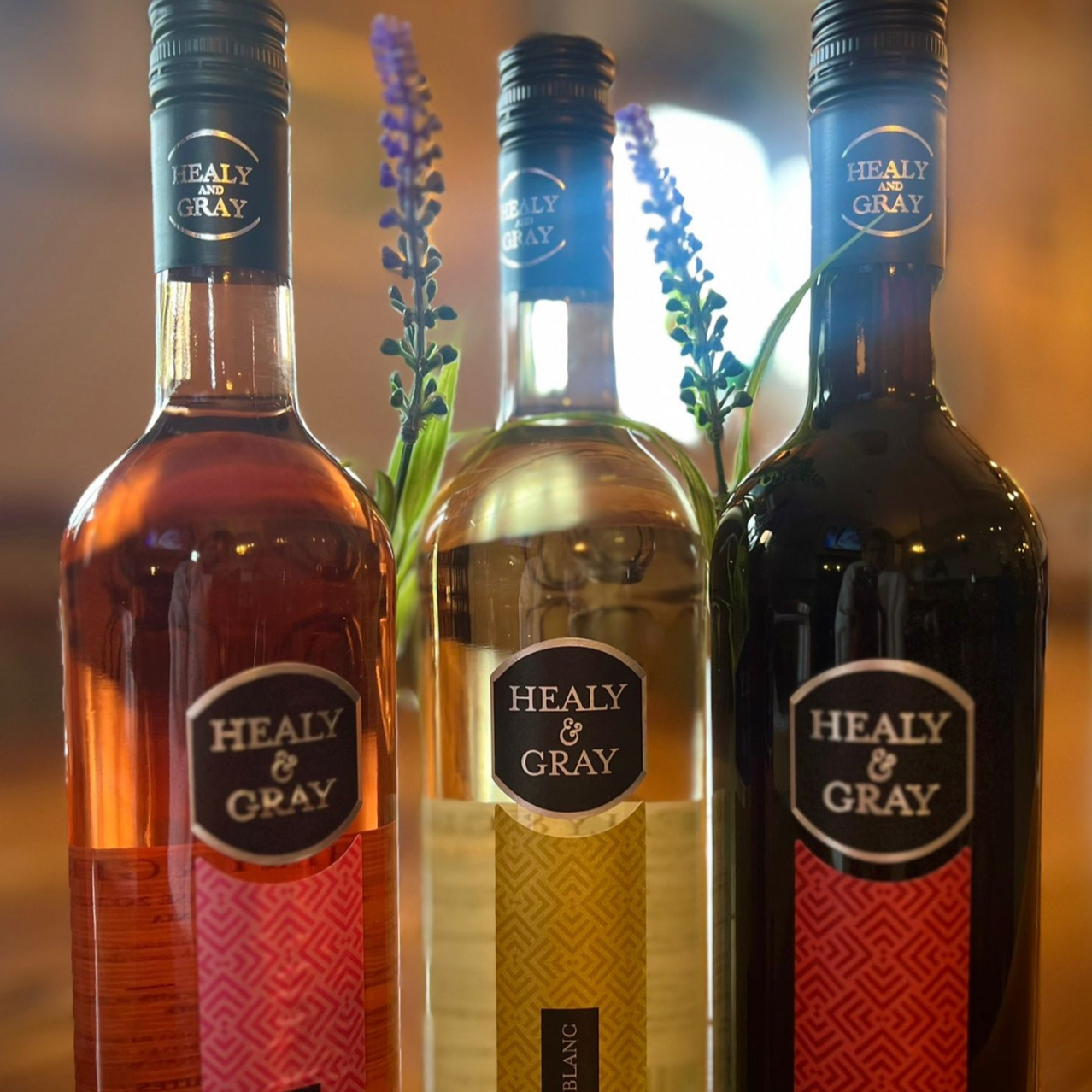 Three bottles of Healy & Gray wine, with sprigs of lavender and a blurred background lighting.