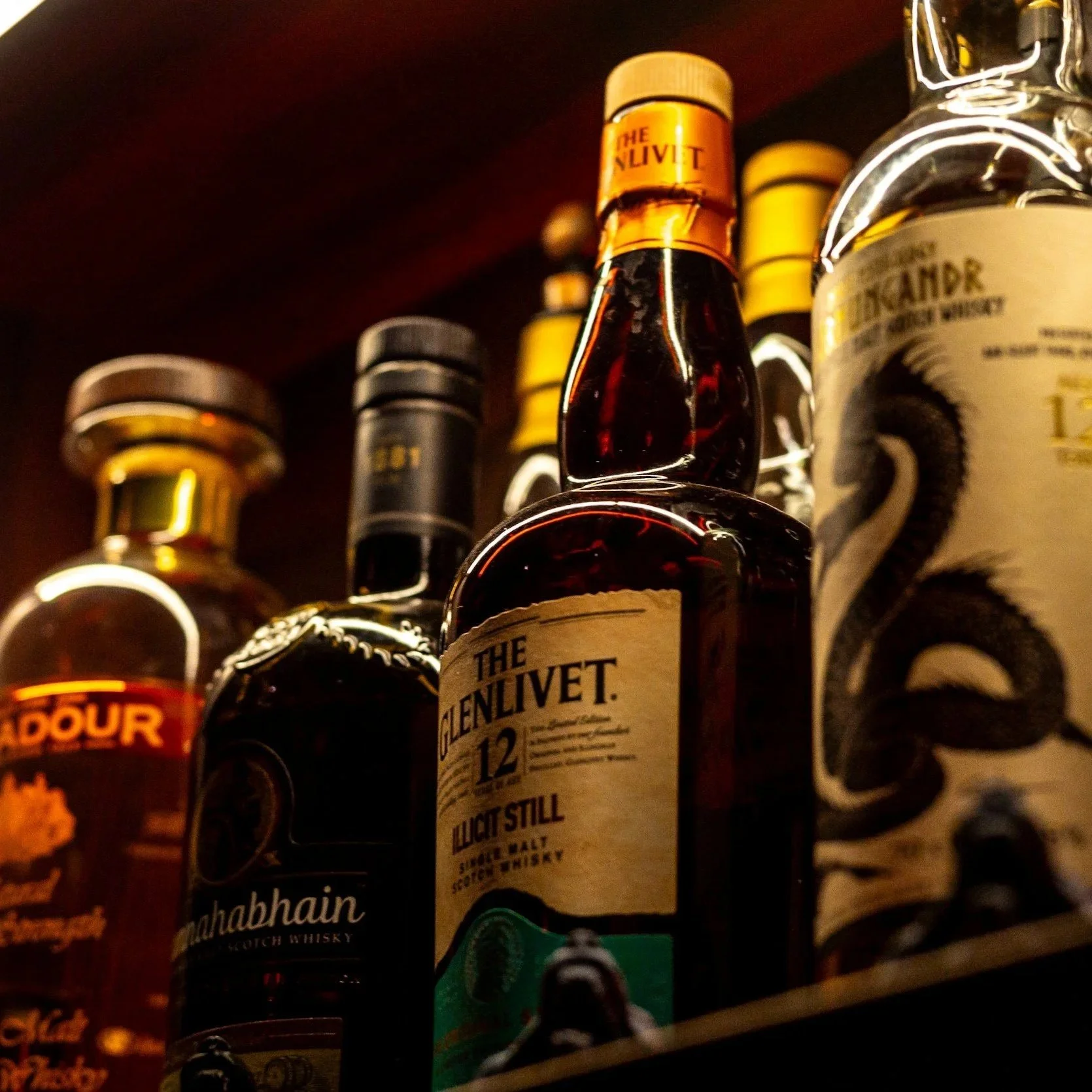 Close-up of a liquor store shelf displaying various bottles of whiskey, including The Glenlivet 12 Year Old single malt Scotch whiskey, with other whiskey brands visible in the background.