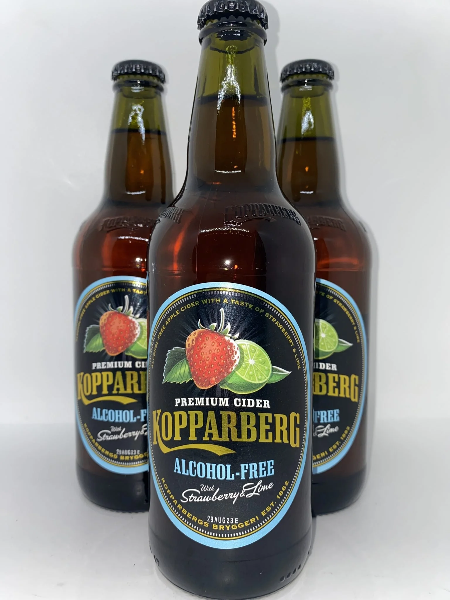 Three bottles of Kopparberg premium cider with strawberry and lime flavor, all standing on a white surface against a plain background.