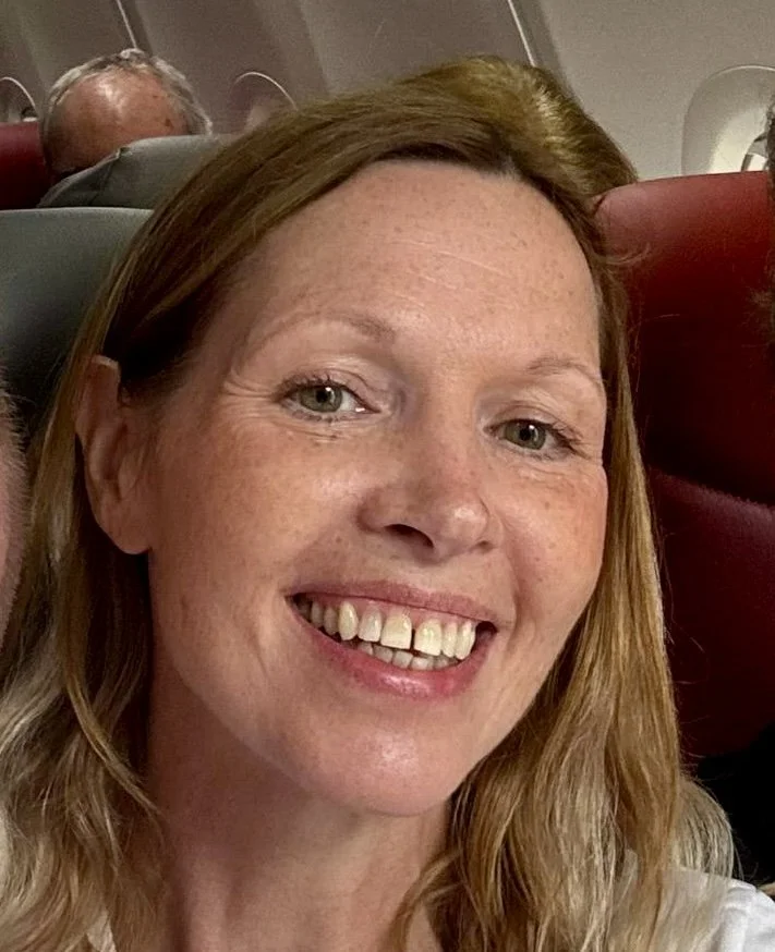 A woman with light brown hair and freckles smiling on an airplane.