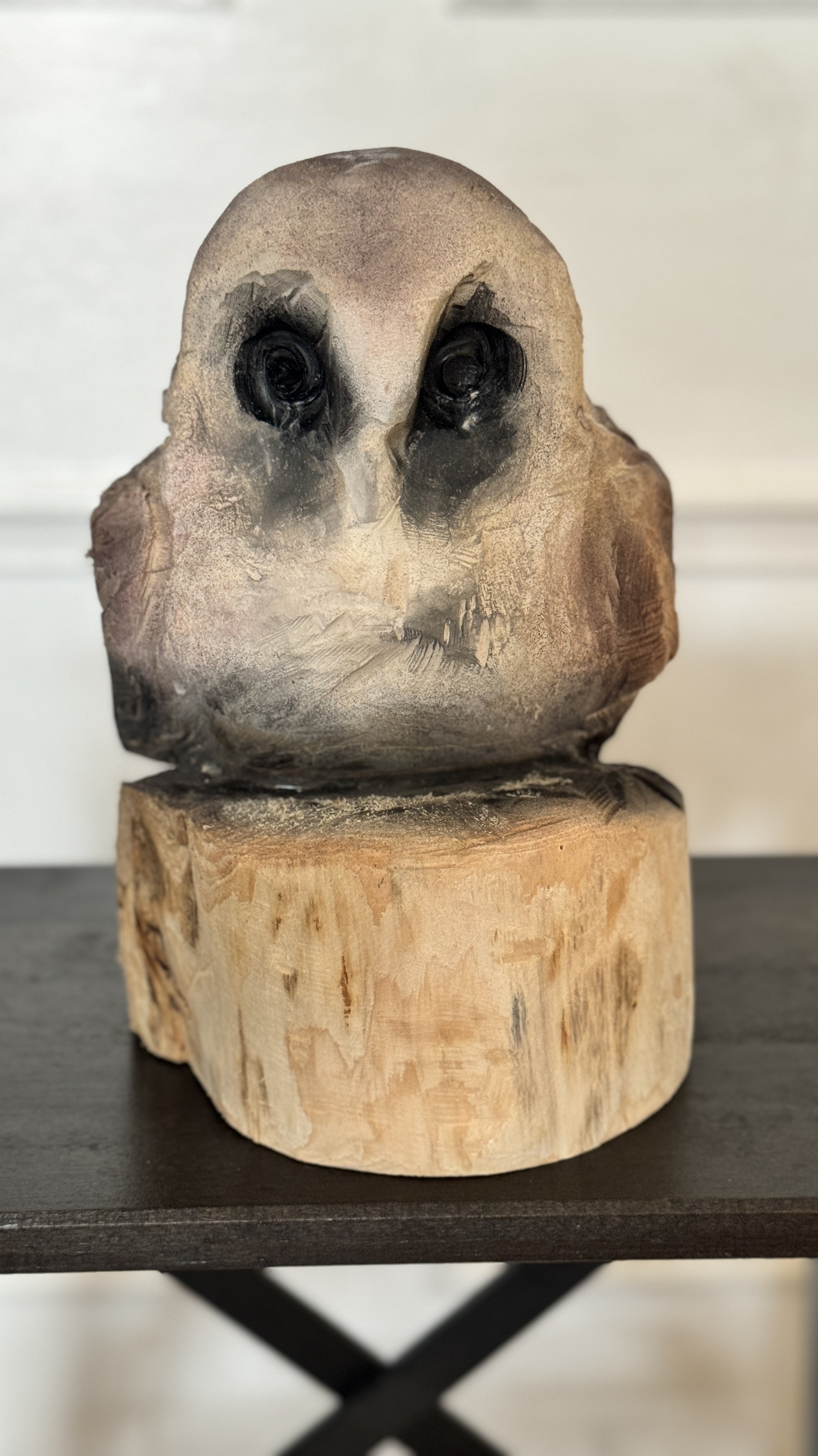 Wooden owl sculpture on a black table with a white wall background.