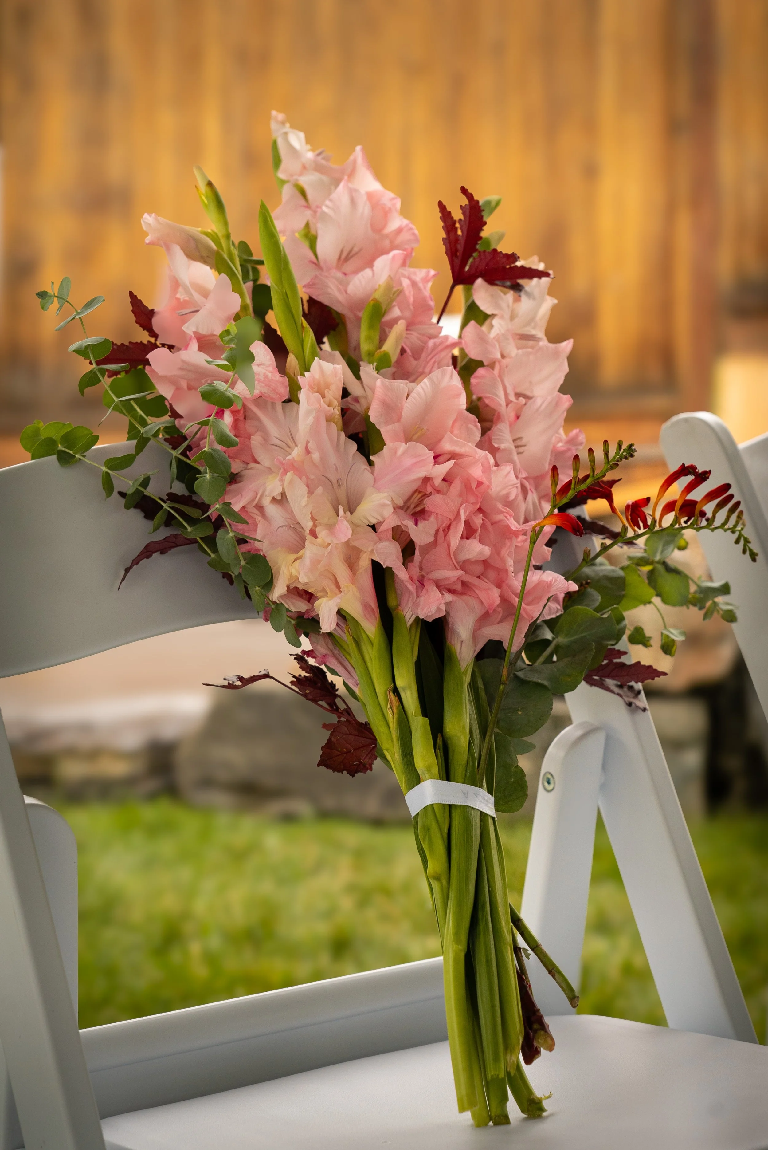A bouquet of pink gladiolus and greenery tied to a white chair