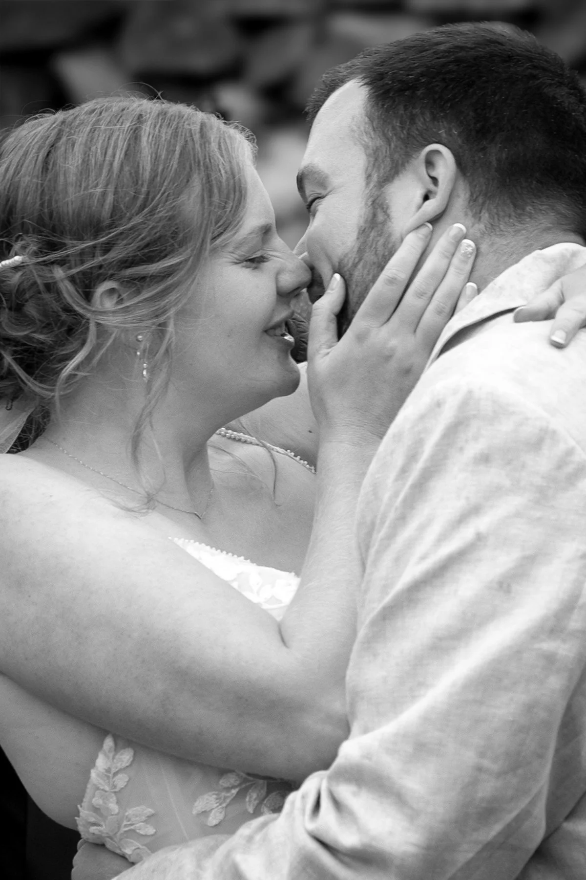 A black and white photo of a couple about to kiss, with the woman gently holding the man's face and their noses touching.