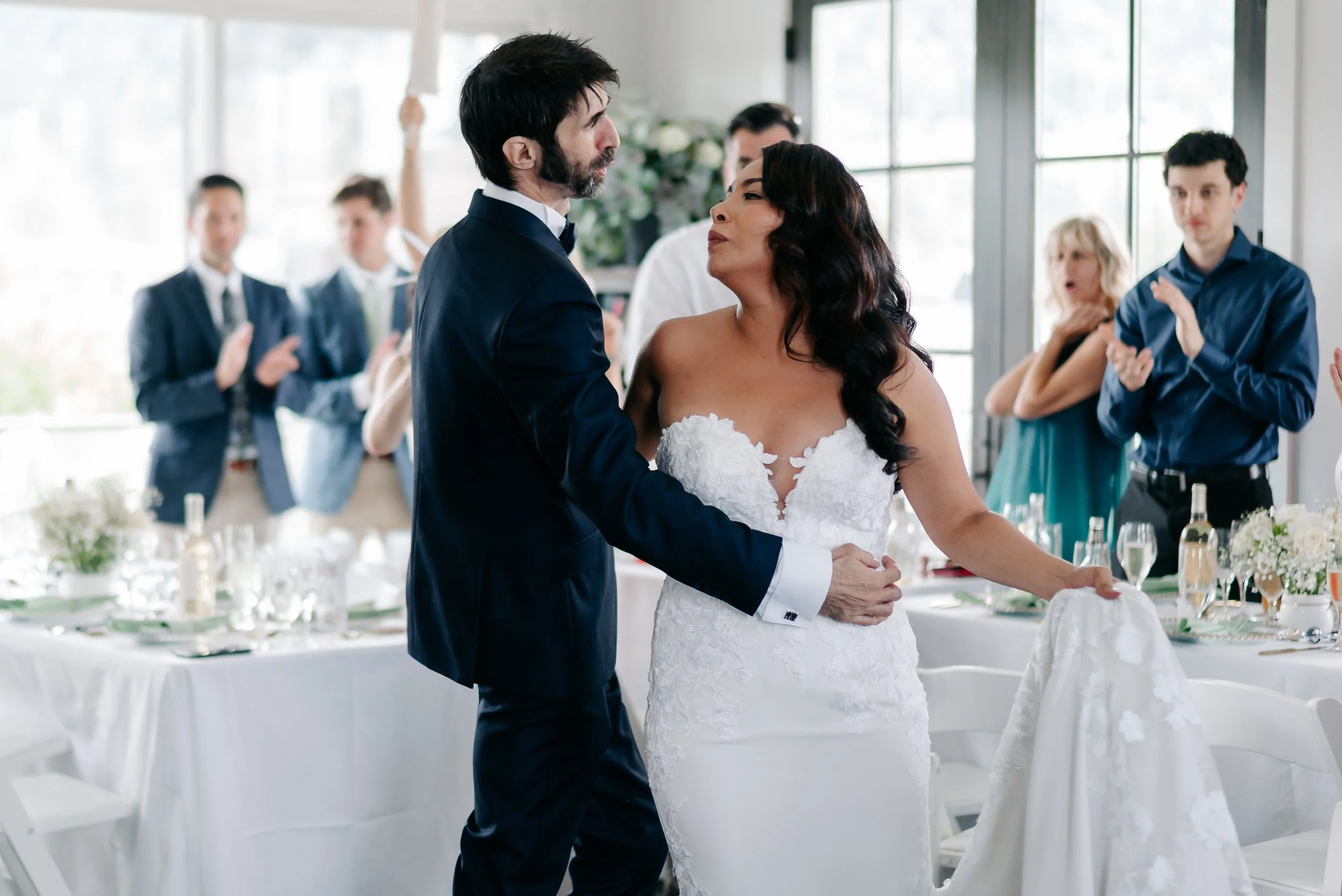 A bride and groom dance at their wedding reception while guests applaud around them.