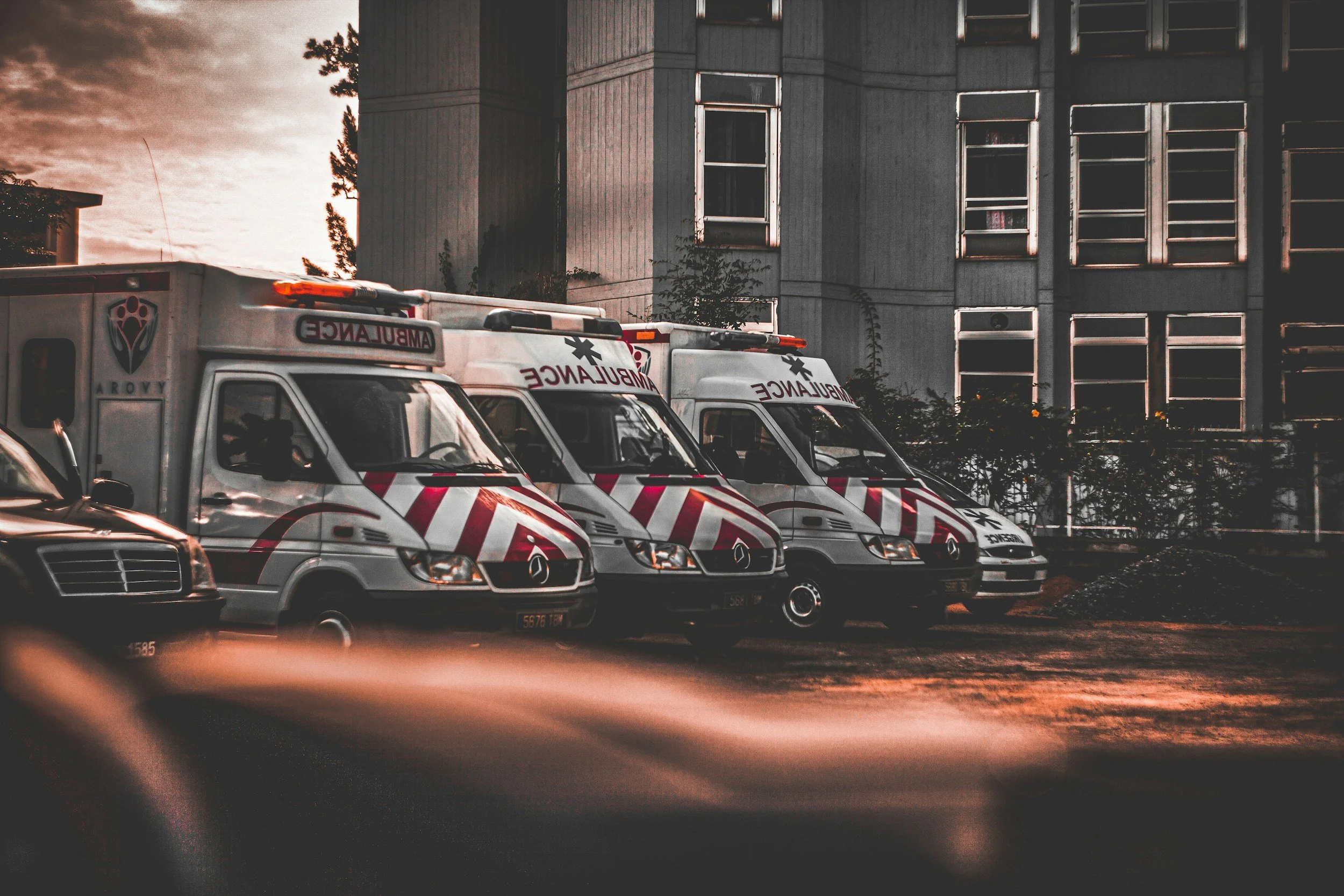 Several ambulances parked in front of a building during dusk.