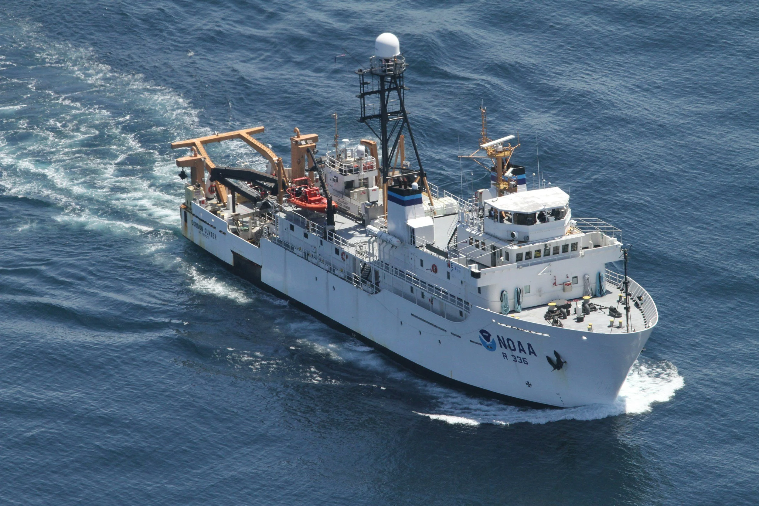 A NOAA research vessel at sea, painted white with the NOAA logo and the call sign R 336 visible on the side, sailing through blue waters.